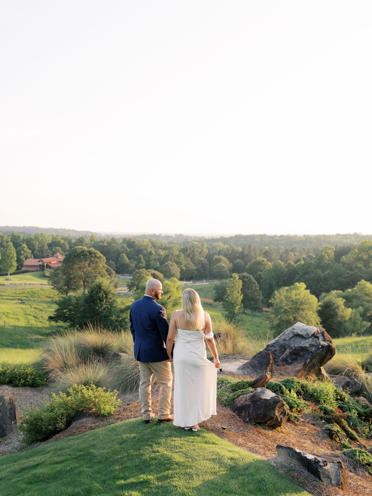 Couple stands together on hilltop overlooking scenic valley at sunset.