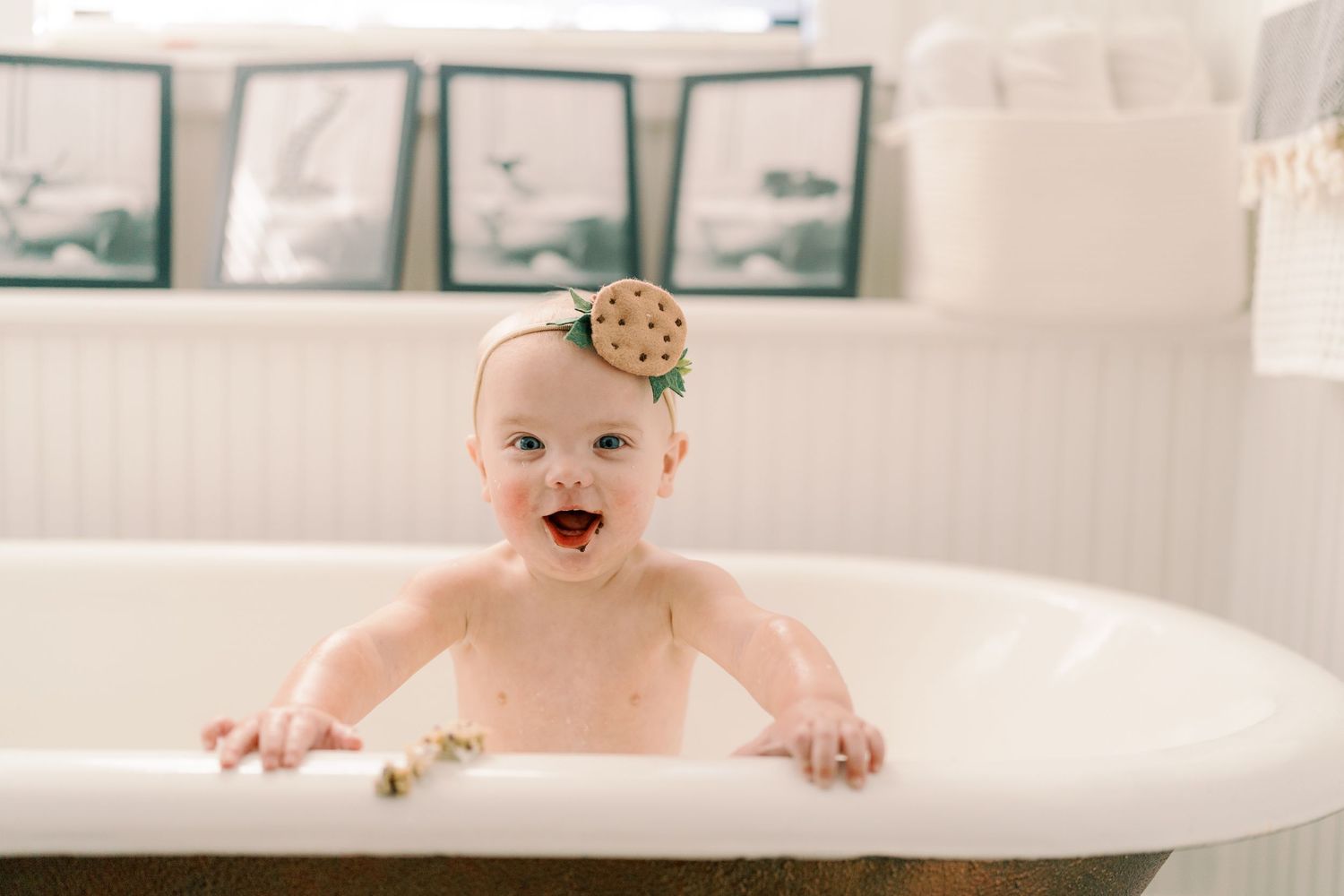 Joyful baby plays in white bathtub with natural light streaming through windows.