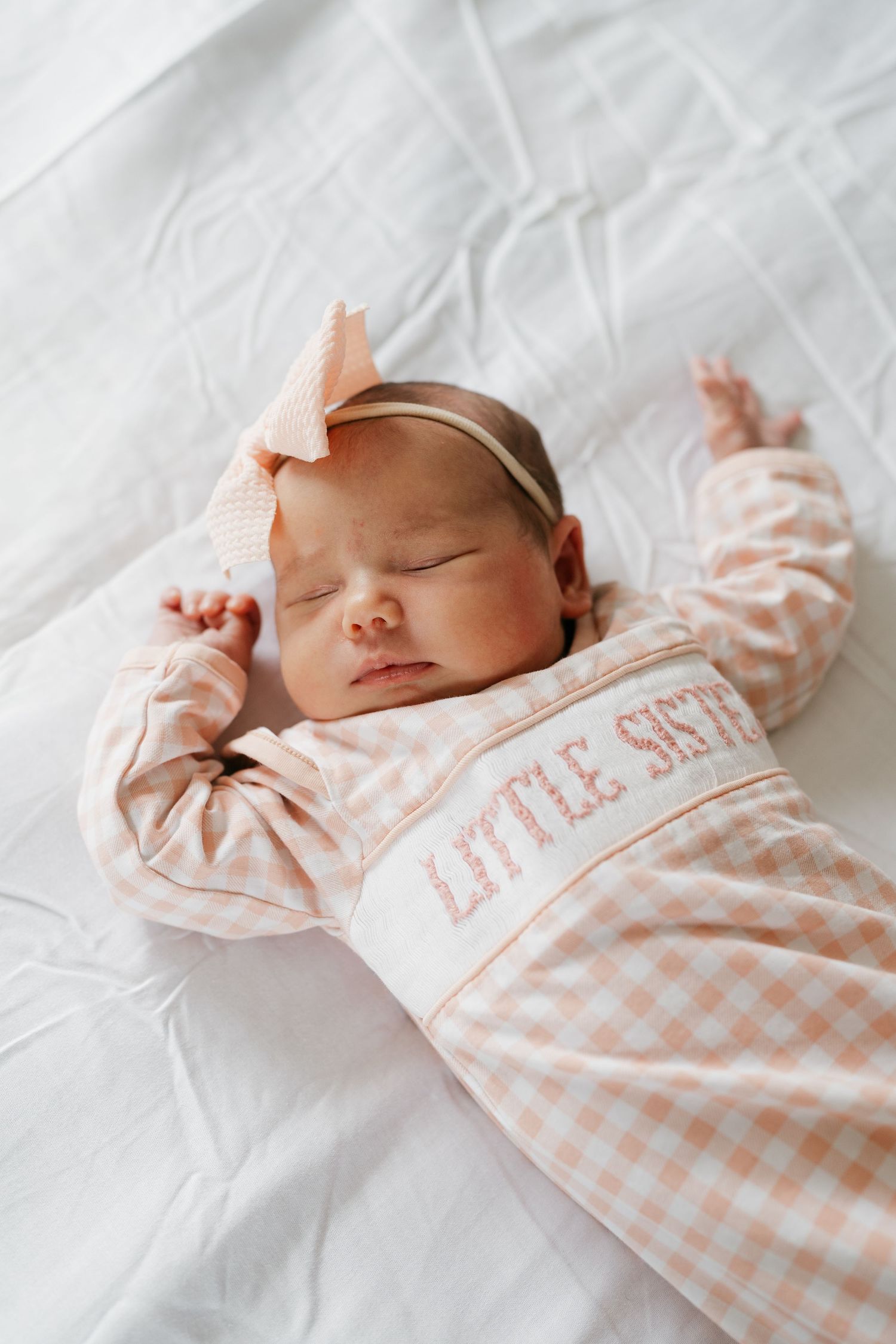 Peaceful sleeping newborn in pink gingham outfit on white bedding.
