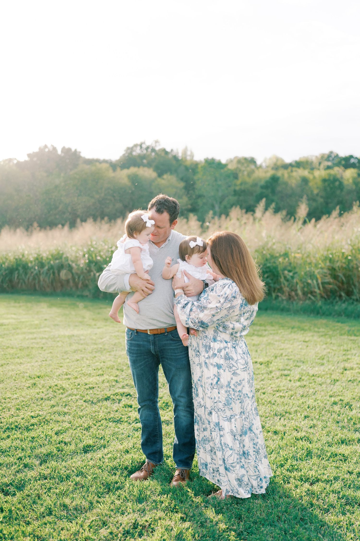 Family enjoying a candid moment together in a sunlit meadow during outdoor photo session.