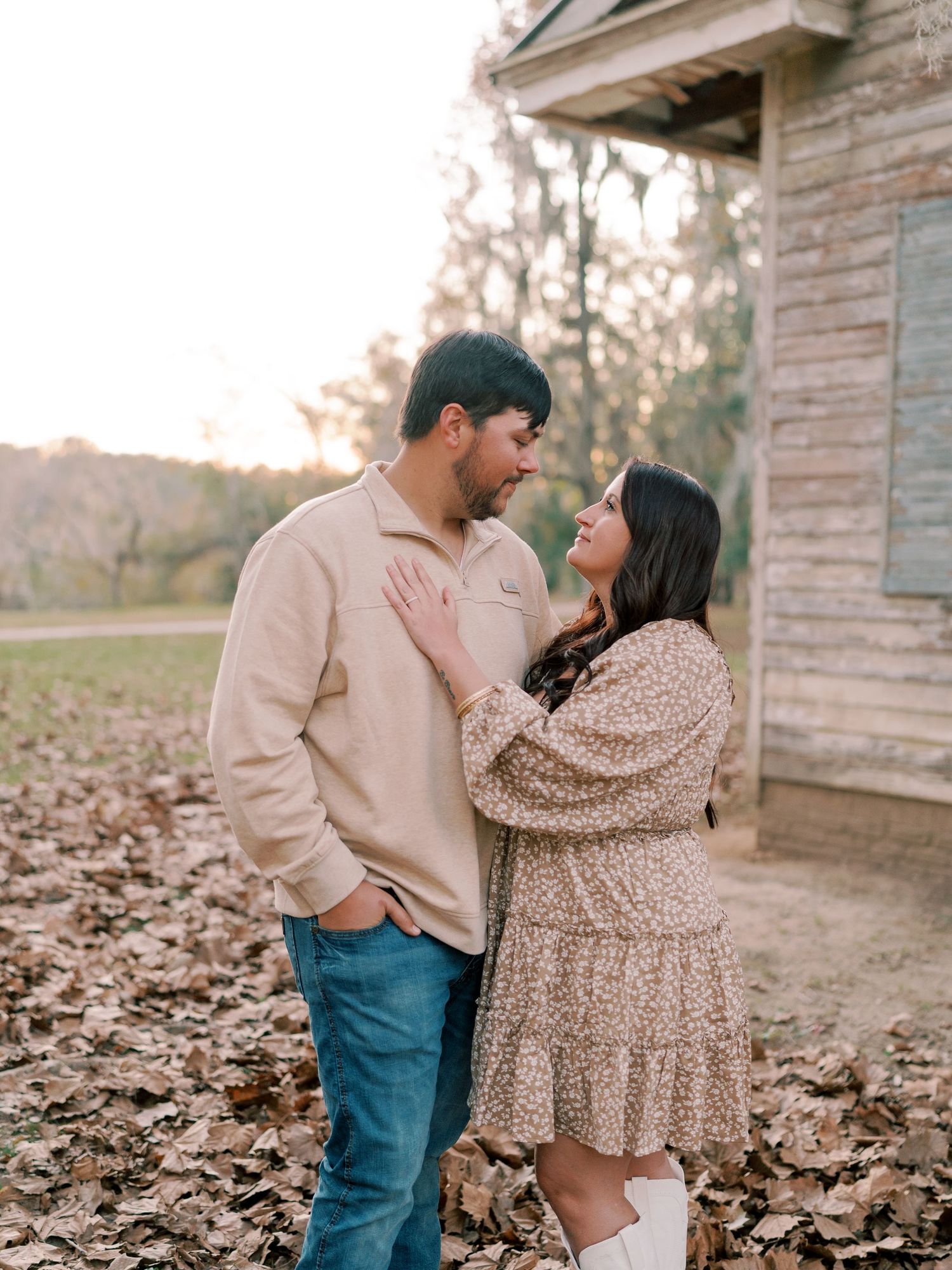A couple in casual attire shares a tender moment among autumn leaves.