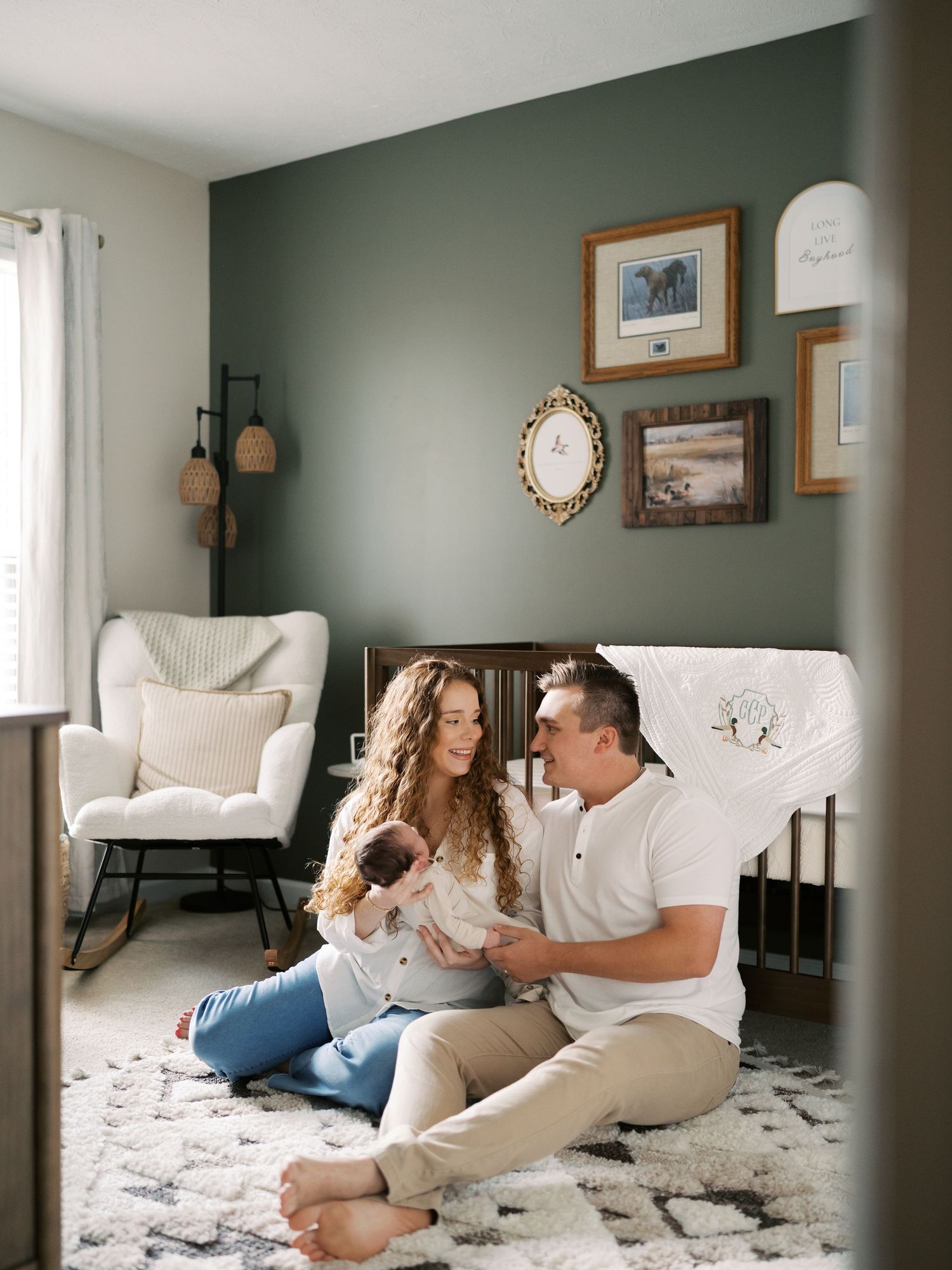 Intimate family moment captured on a soft white rug in a sage green nursery.