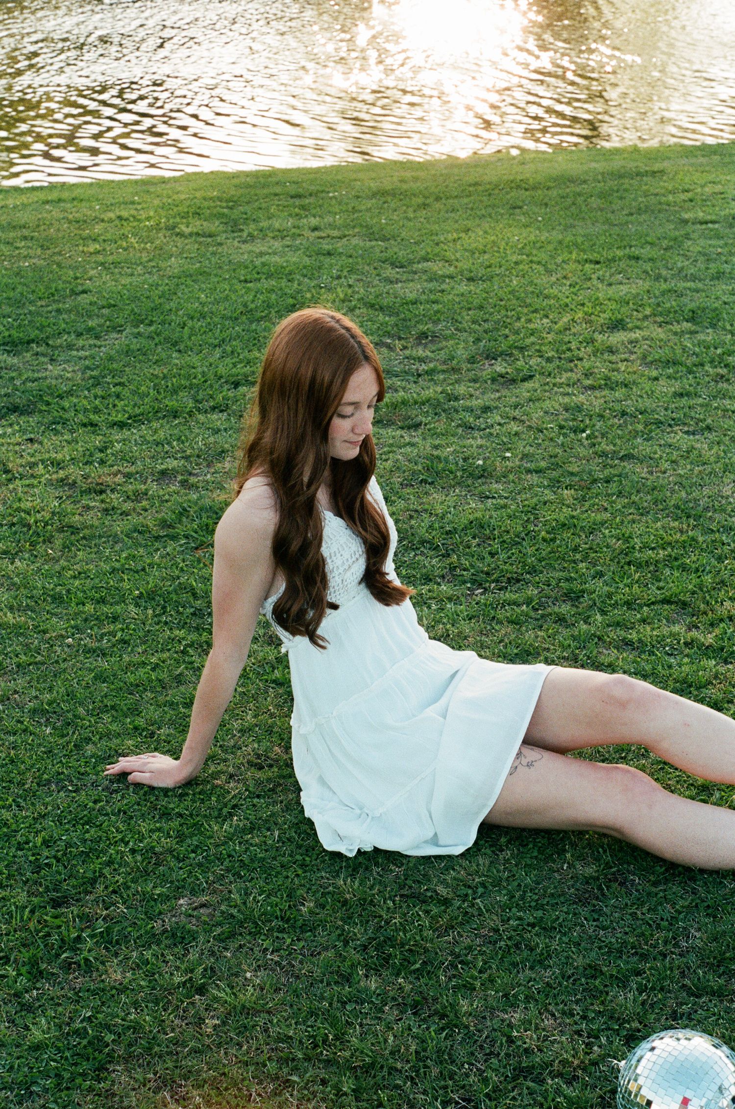 Portrait session by a lake showing relaxed poses in white dress on grass.