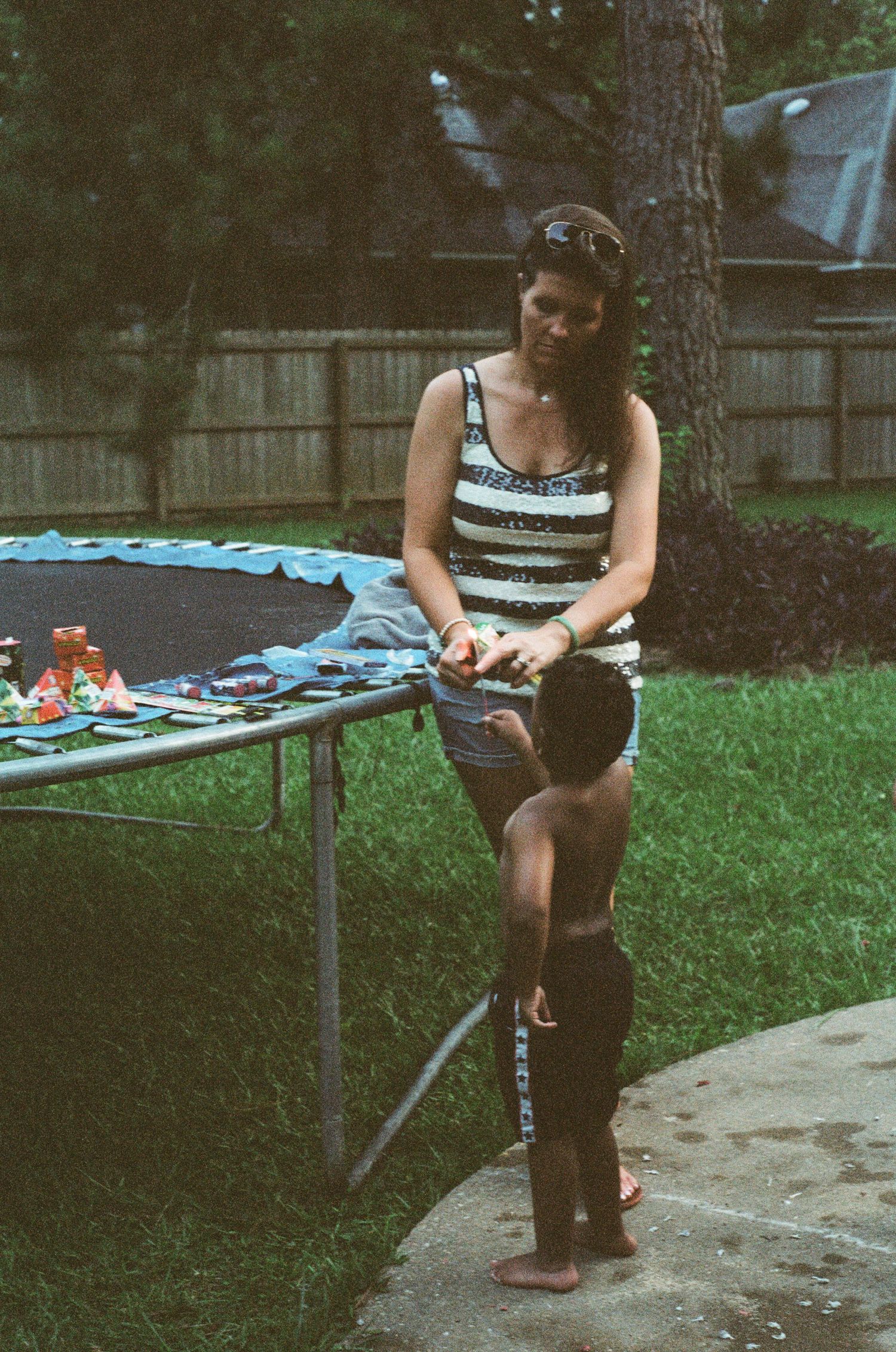 Person sitting on a trampoline in a backyard setting during twilight hours.