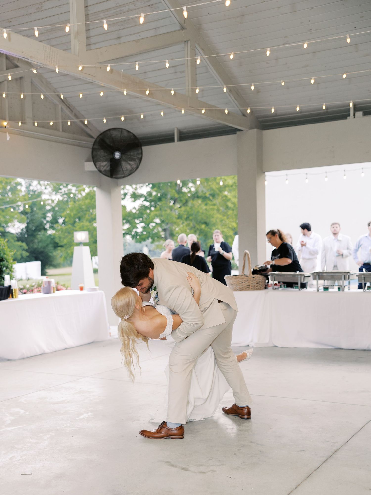 Romantic dance dip during wedding reception under string lights.