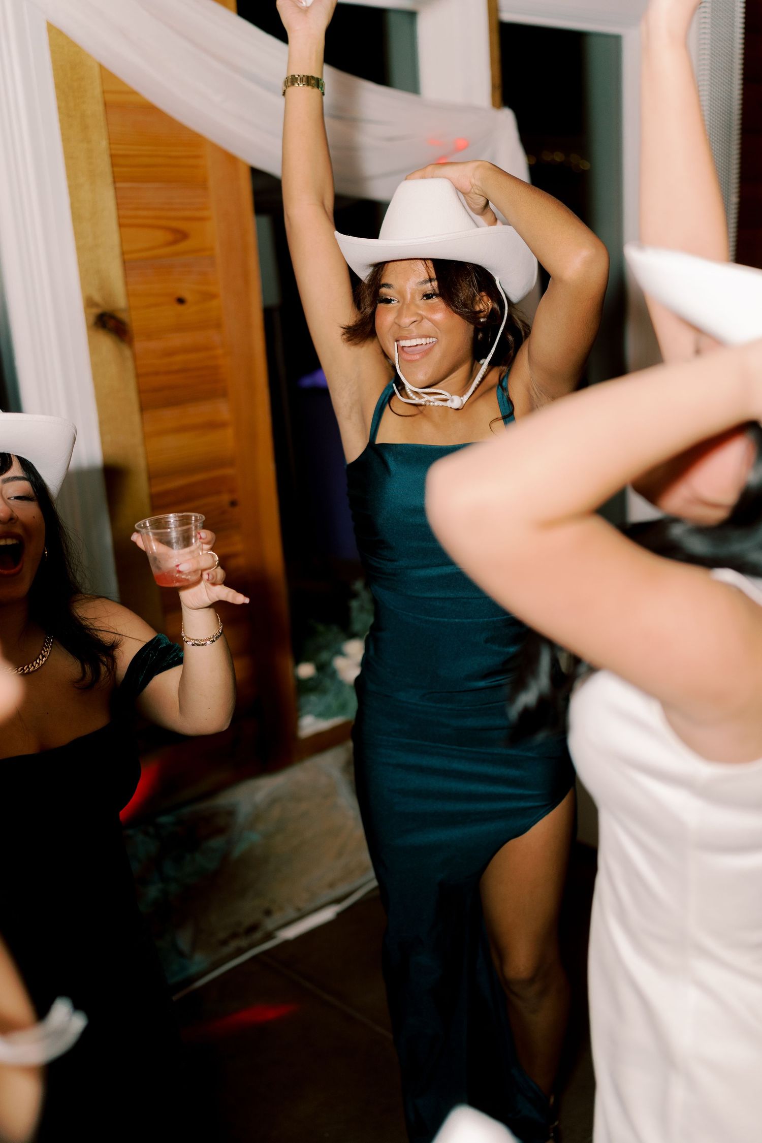 People dancing and celebrating at a party wearing white cowboy hats and dark dresses.