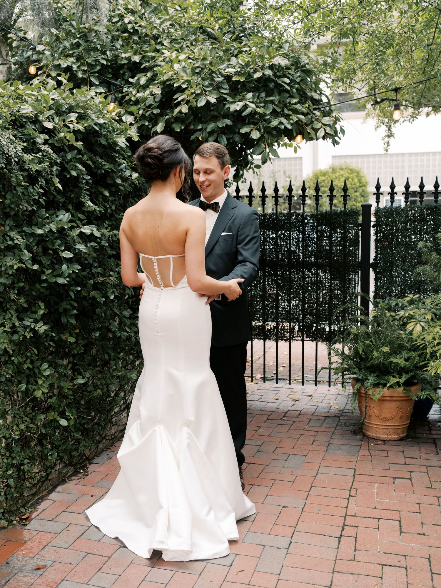 Brick patio surrounded by lush greenery and wrought iron fencing.