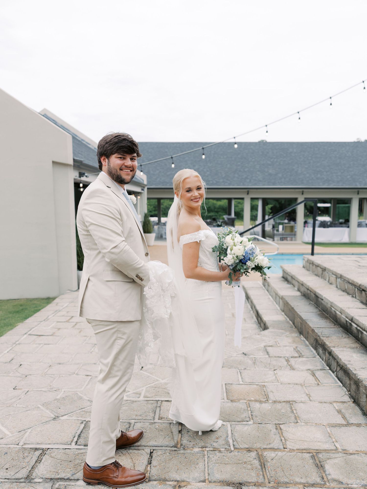 Wedding couple posing on stone steps outside a white building.
