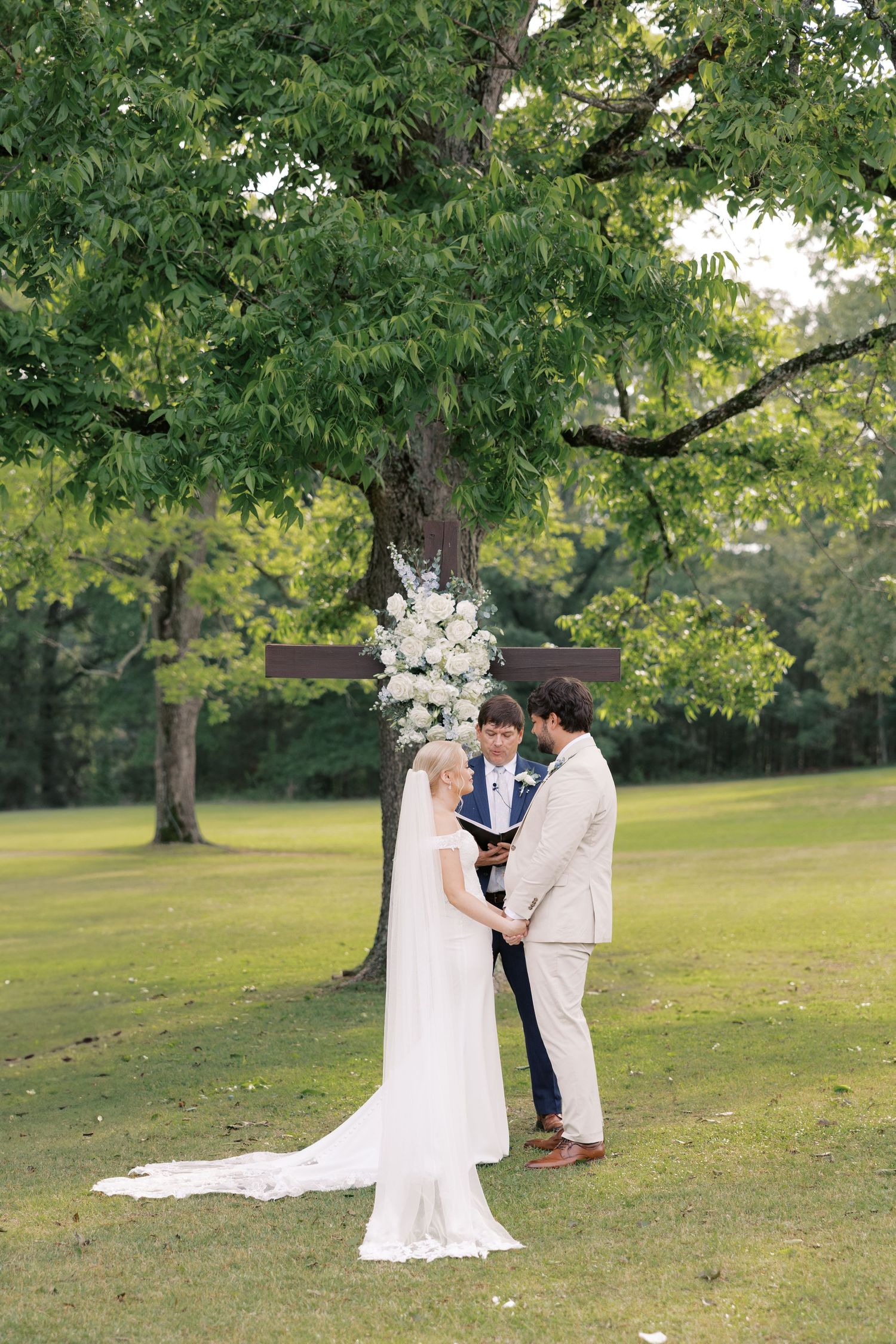 A couple shares an intimate moment during their outdoor wedding ceremony under green trees.