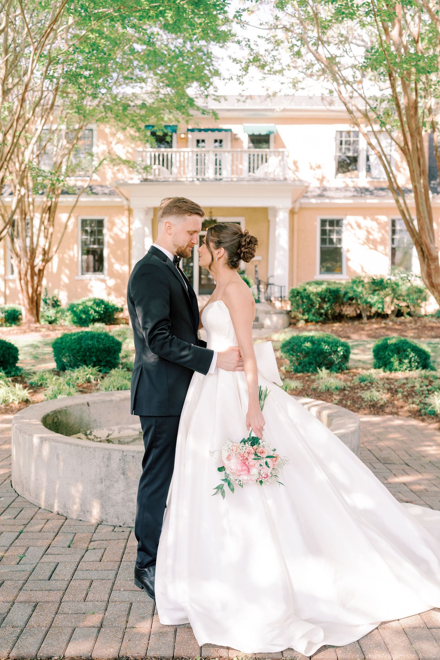 Romantic wedding portraits on a brick patio with landscaped garden and colonial building backdrop.