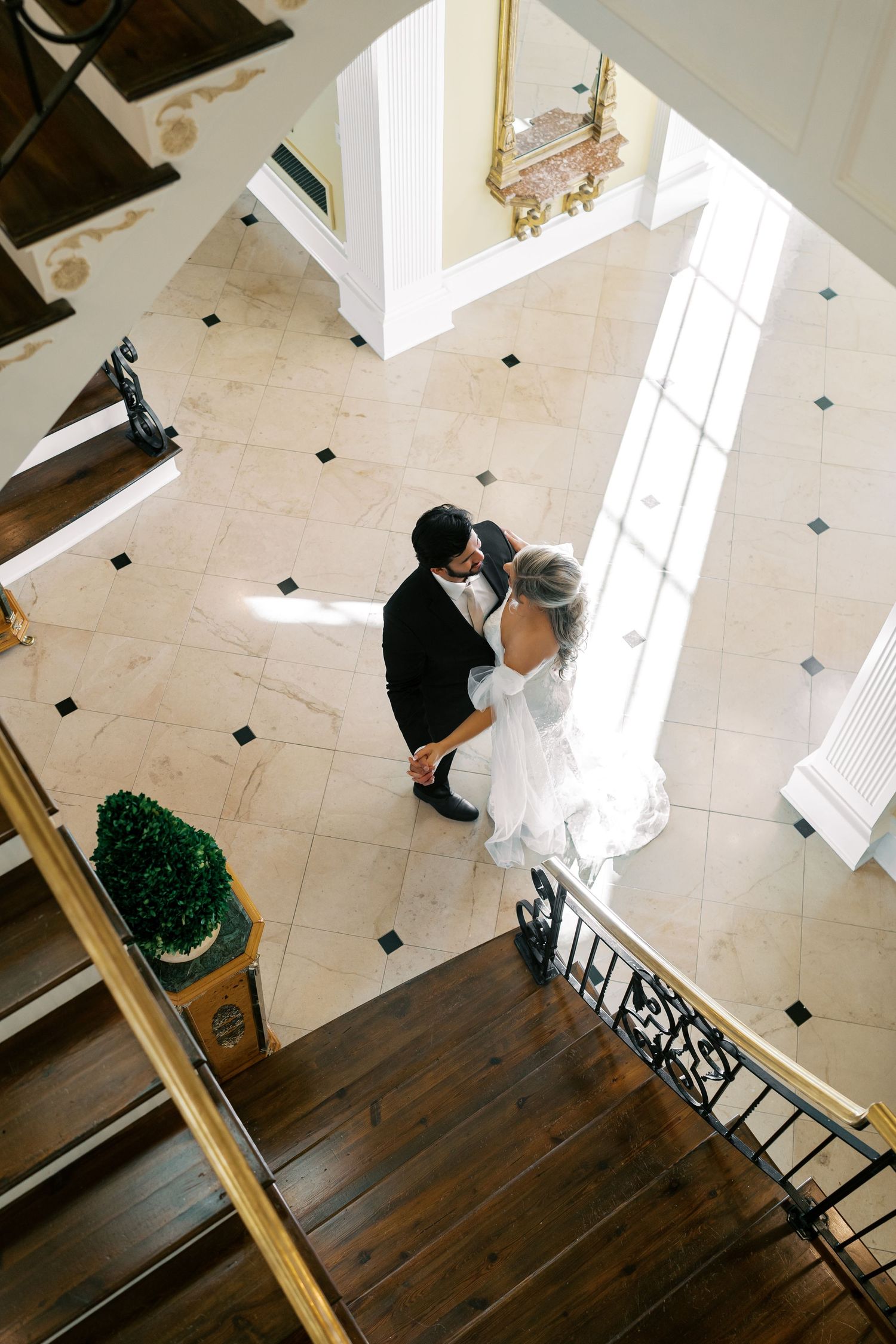 Aerial view of wedding couple on grand staircase with ornate details and marble floors.