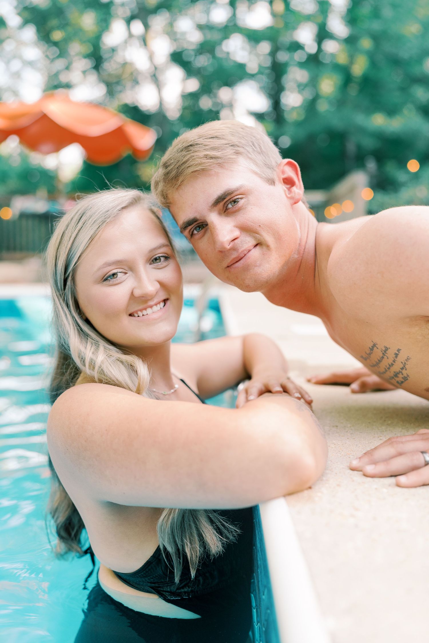 A couple shares a romantic moment at the edge of a swimming pool on a sunny day.
