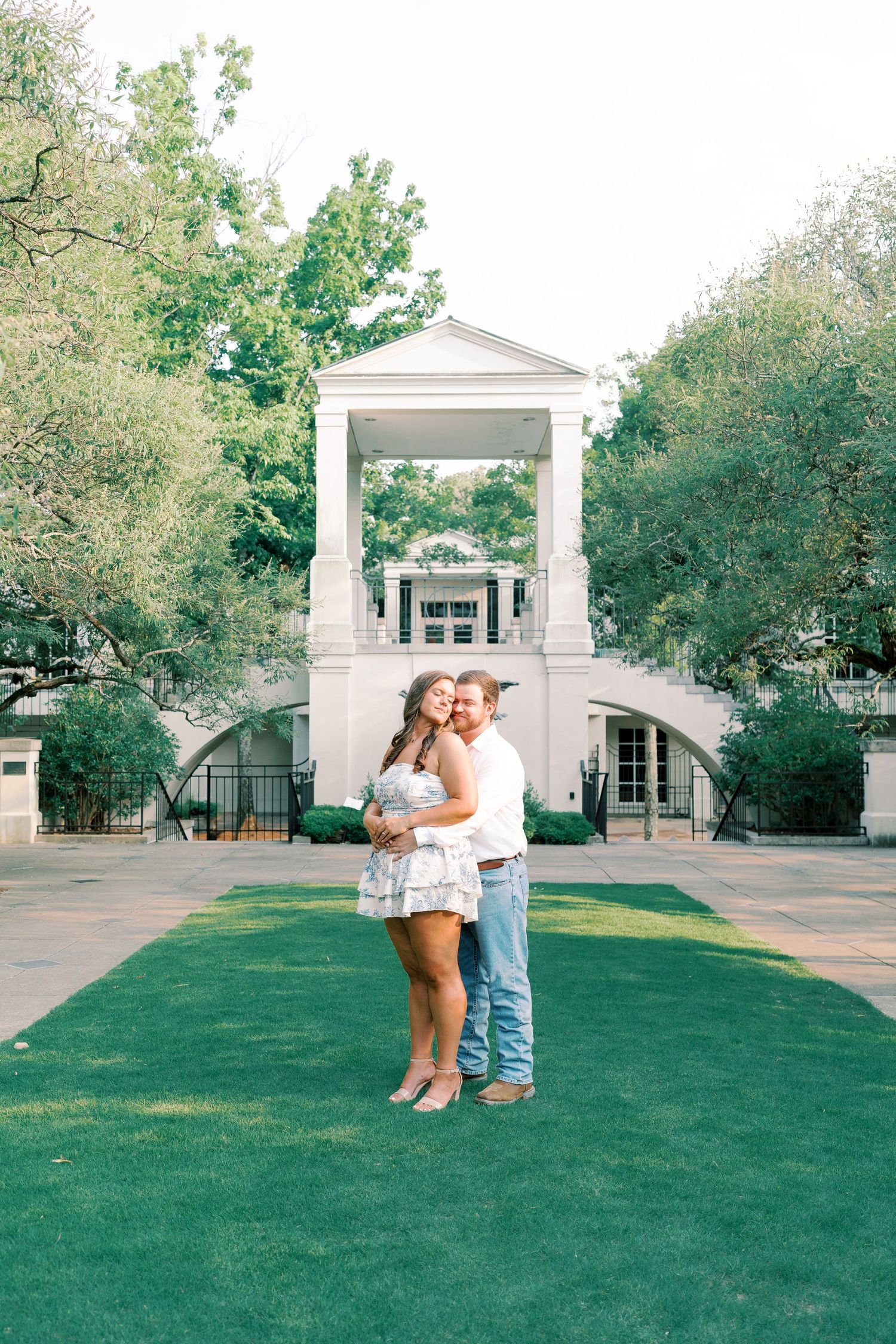 A couple poses together on a manicured lawn in front of a white columned building.