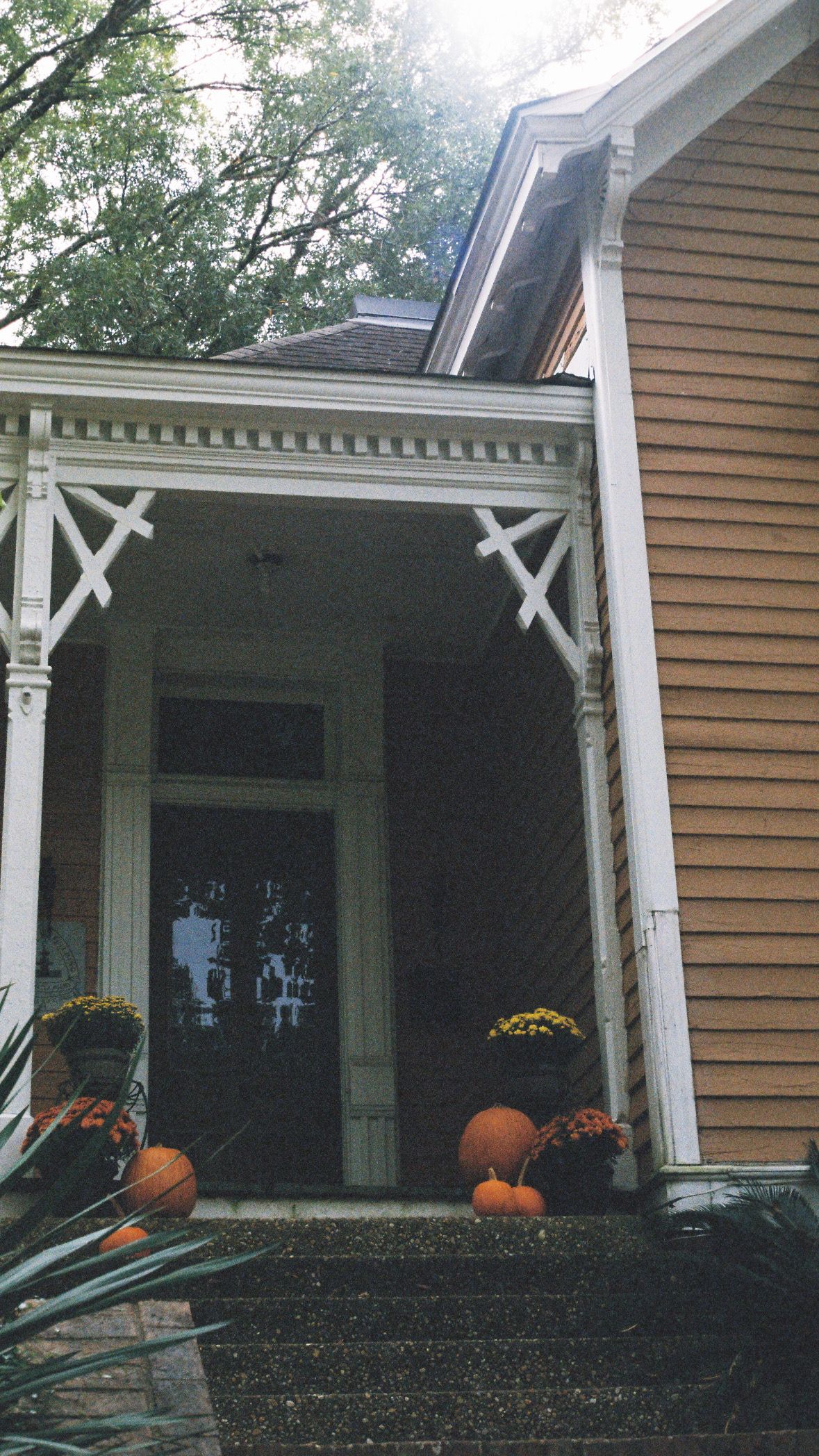 Fall decorations with pumpkins on the front porch of a tan house with white trim.