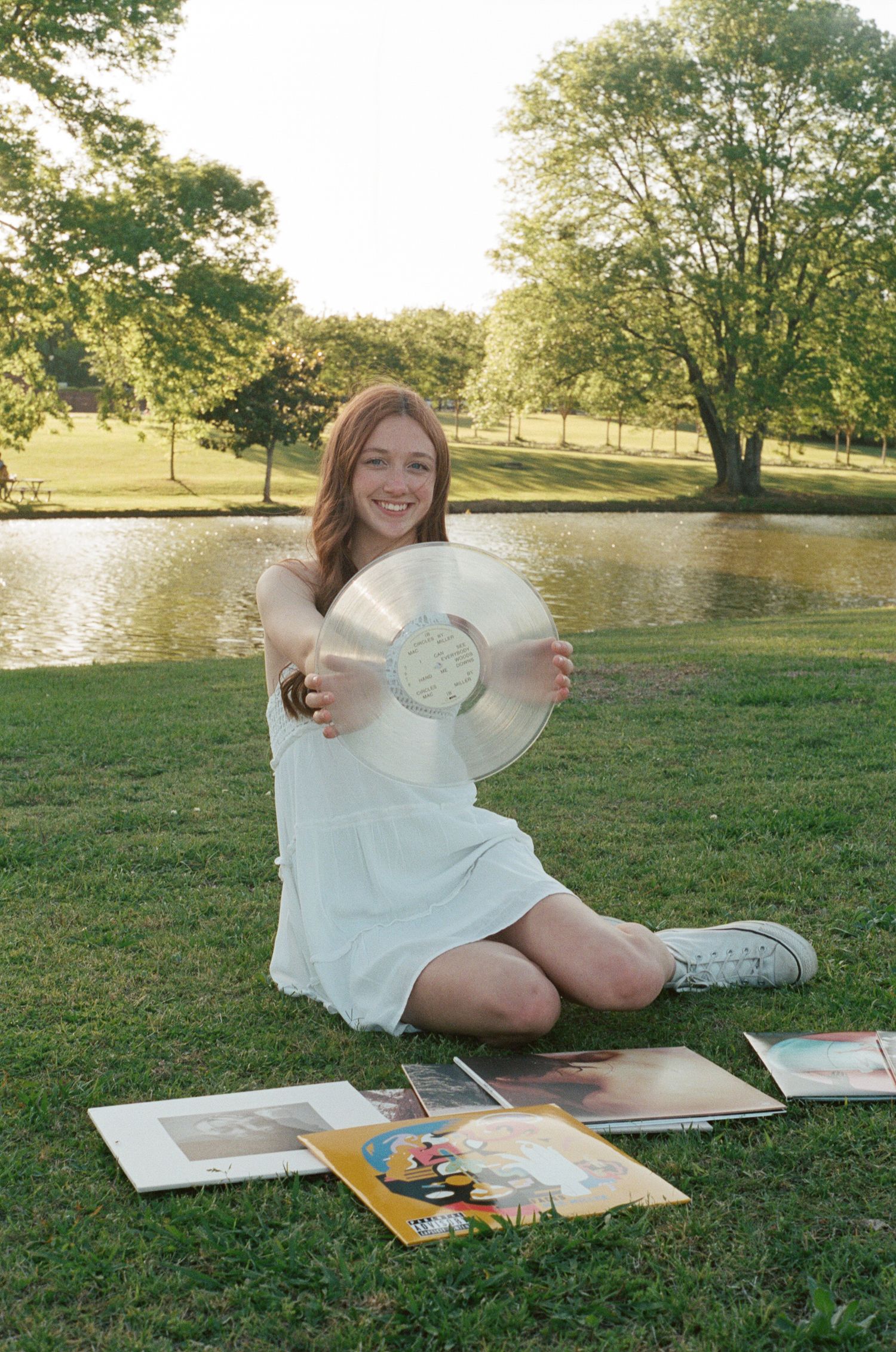 Outdoor photo session with vinyl records and books laid out on grass in golden sunlight.