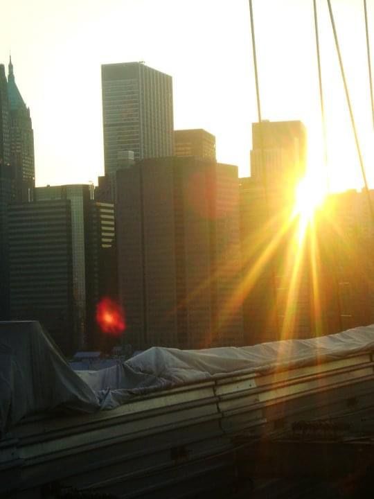 Dramatic sunset behind city skyline with golden sunburst between buildings.