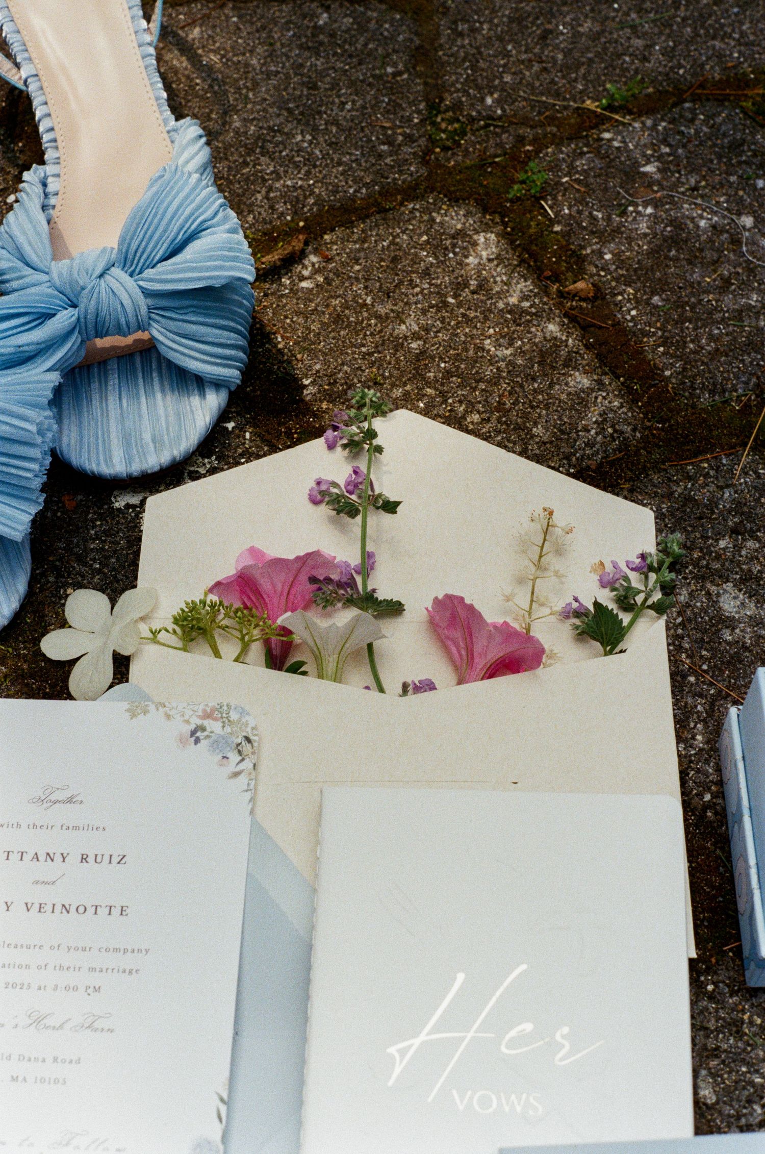 Wedding invitations with light blue ribbons and pink flowers arranged on a stone surface.