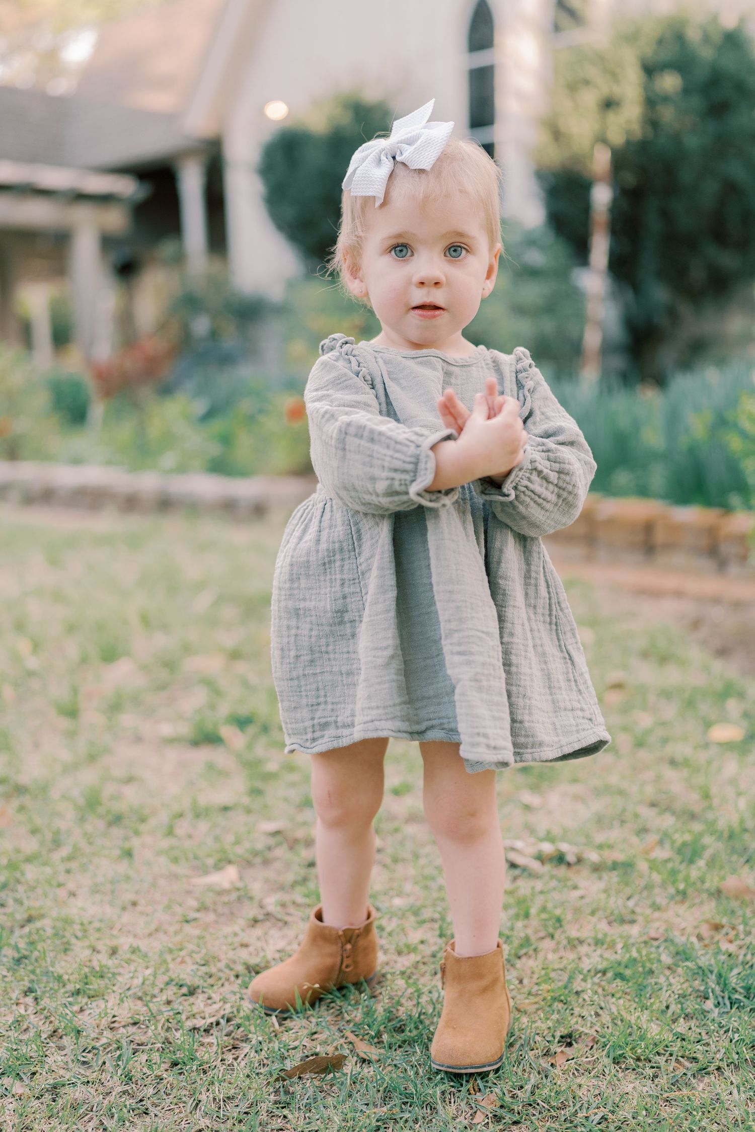 Small feet in brown boots peek out from under a gray dress on grassy ground.