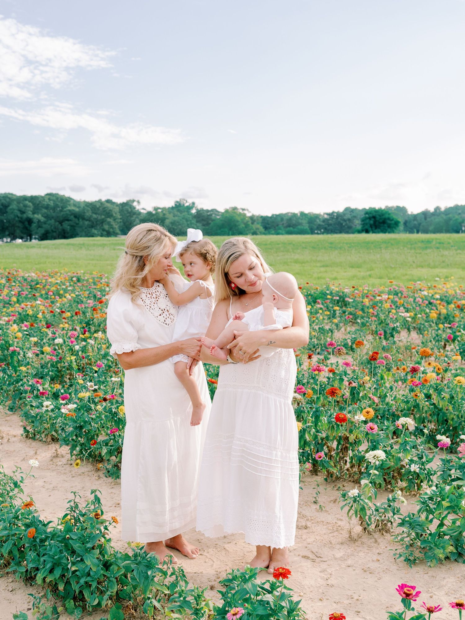Two people in white dresses share joyful moments among colorful wildflowers in a sunny field.