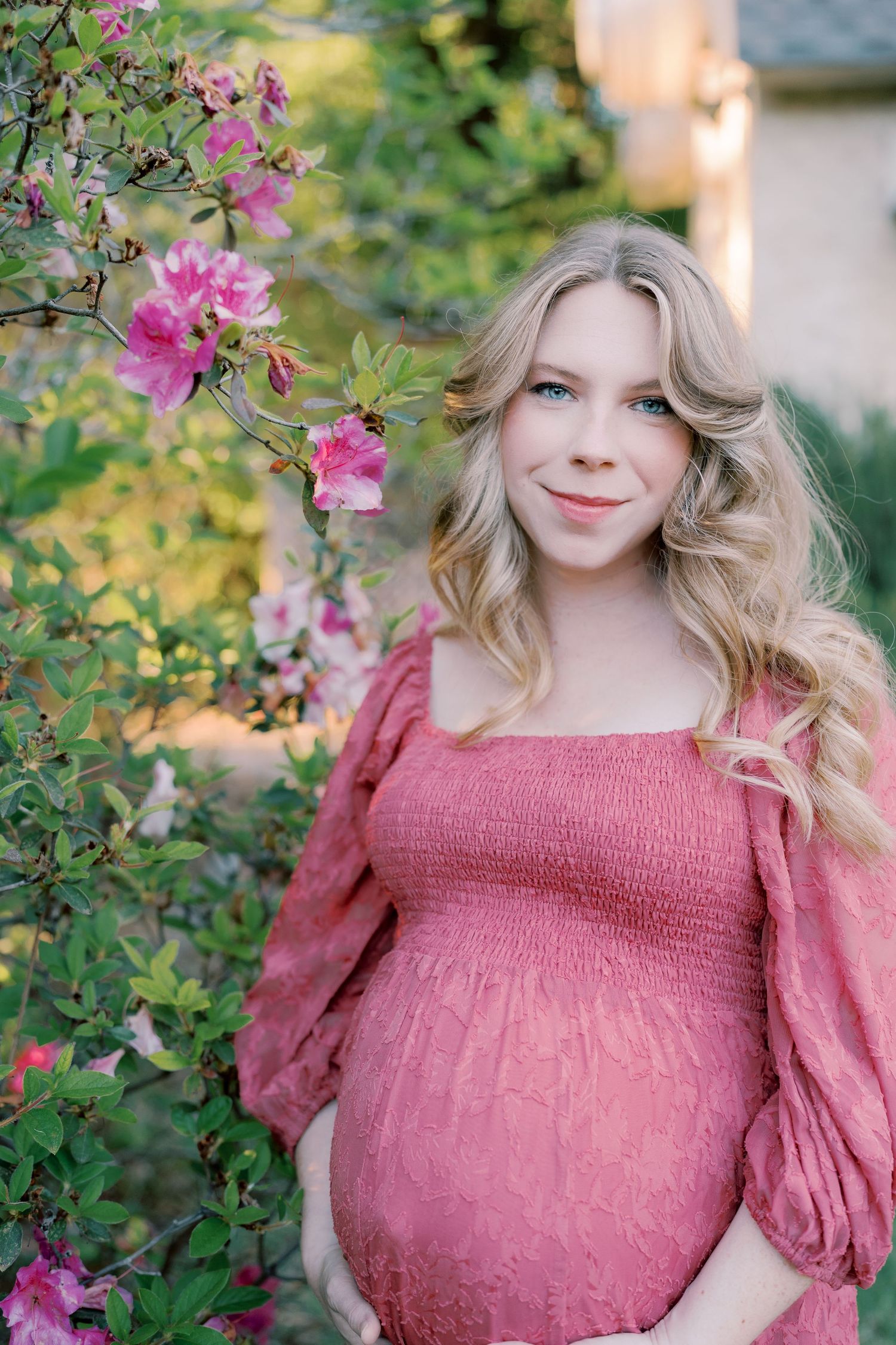 A pink smocked dress is photographed among blooming azalea bushes in a garden setting.