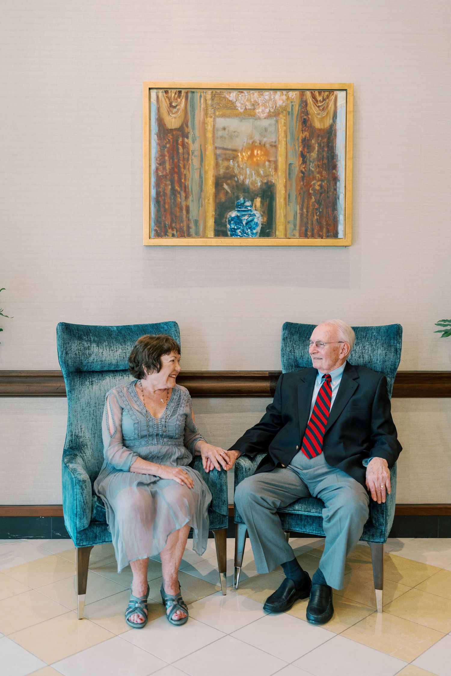 Two people sitting and chatting on teal couch in bright lobby with artwork.