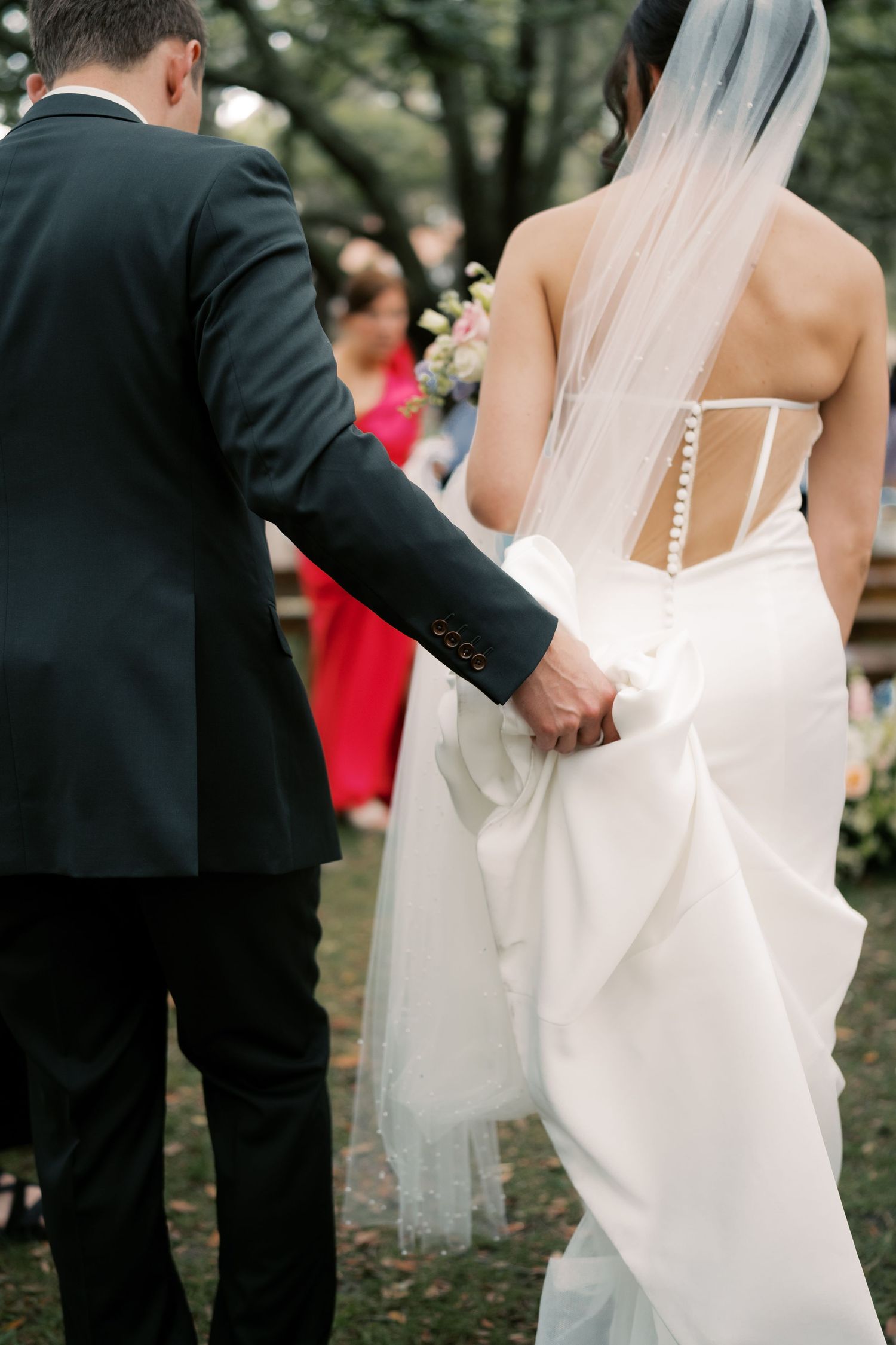 Close-up details of a white wedding dress being buttoned up in an outdoor setting.