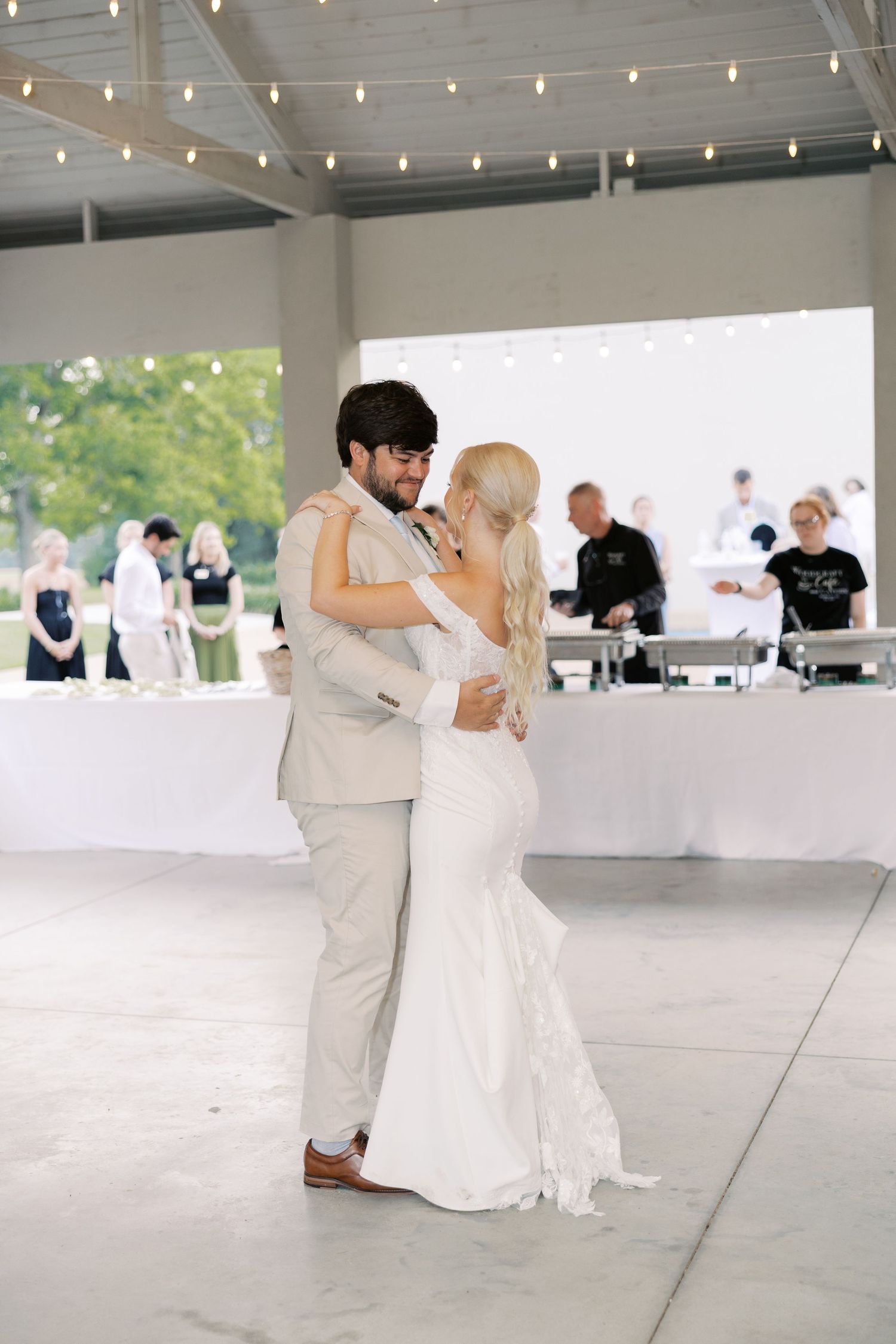 Couple sharing their first dance under string lights at modern outdoor reception venue.