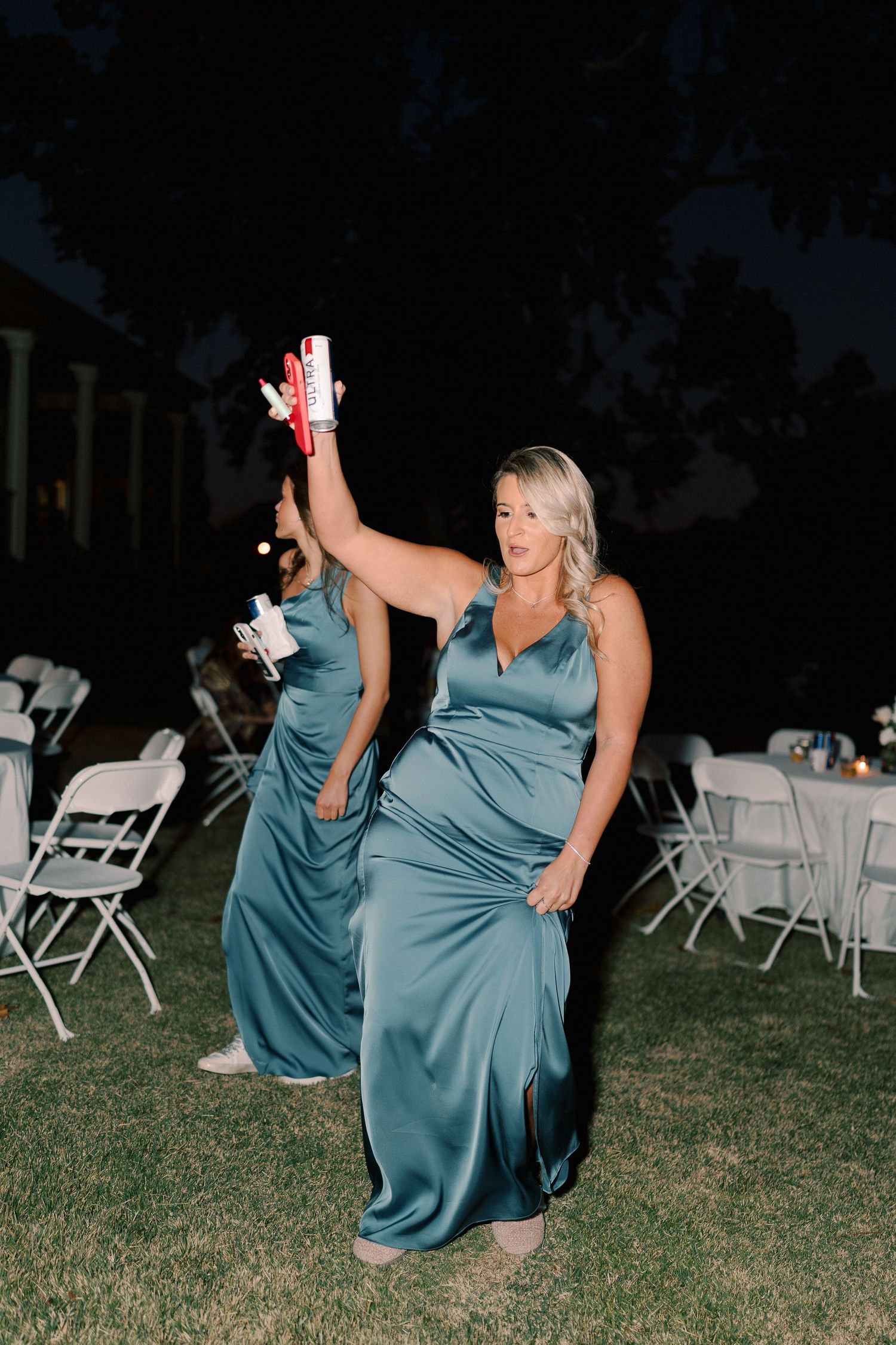 Wedding party members in teal dresses dancing on grass at an outdoor reception.