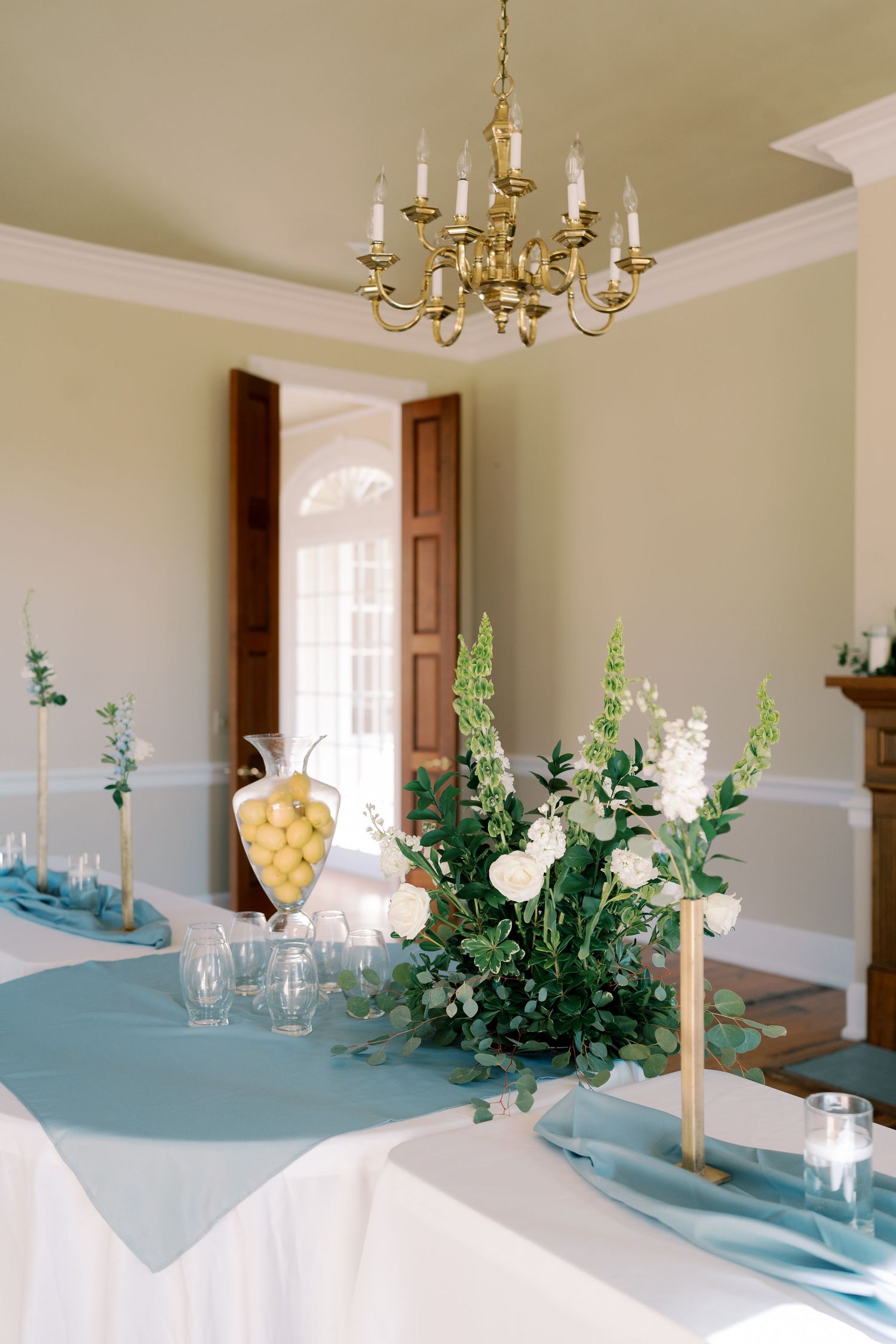Elegant dining room with brass chandelier and table decorated with blue runners and white floral arrangements.