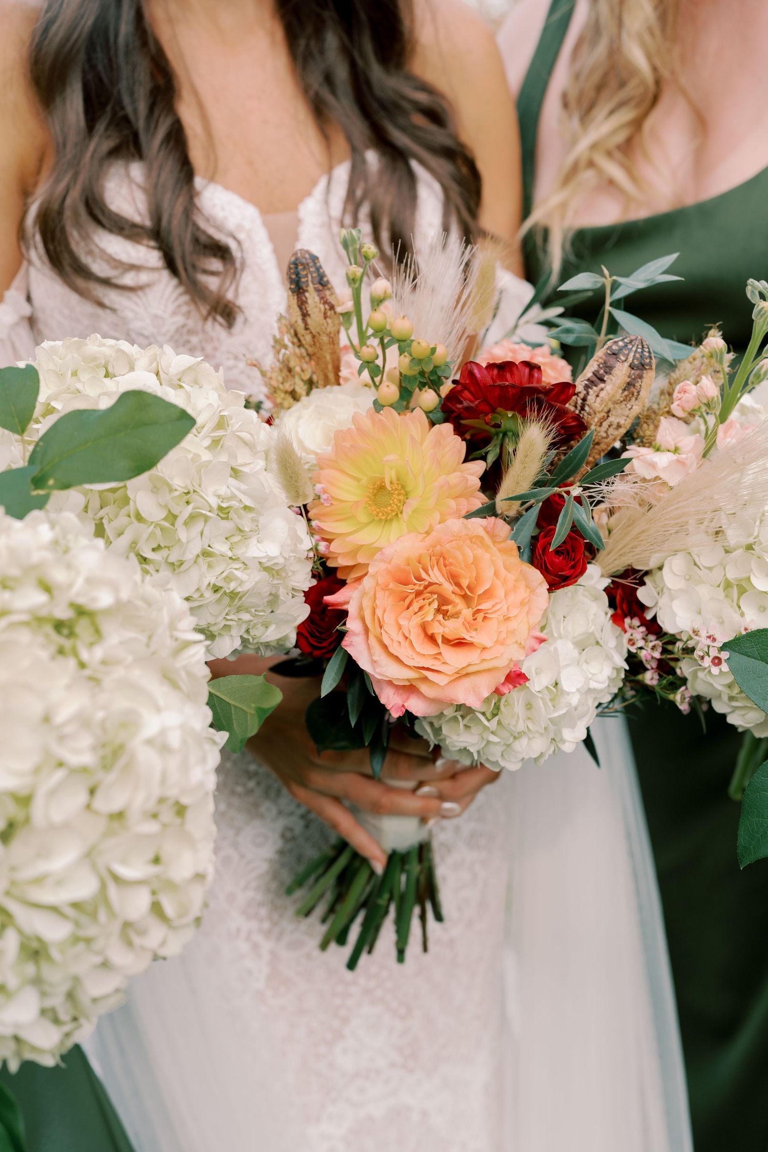 Wedding party holding elegant bouquets with white hydrangeas, peach roses, and burgundy accents.