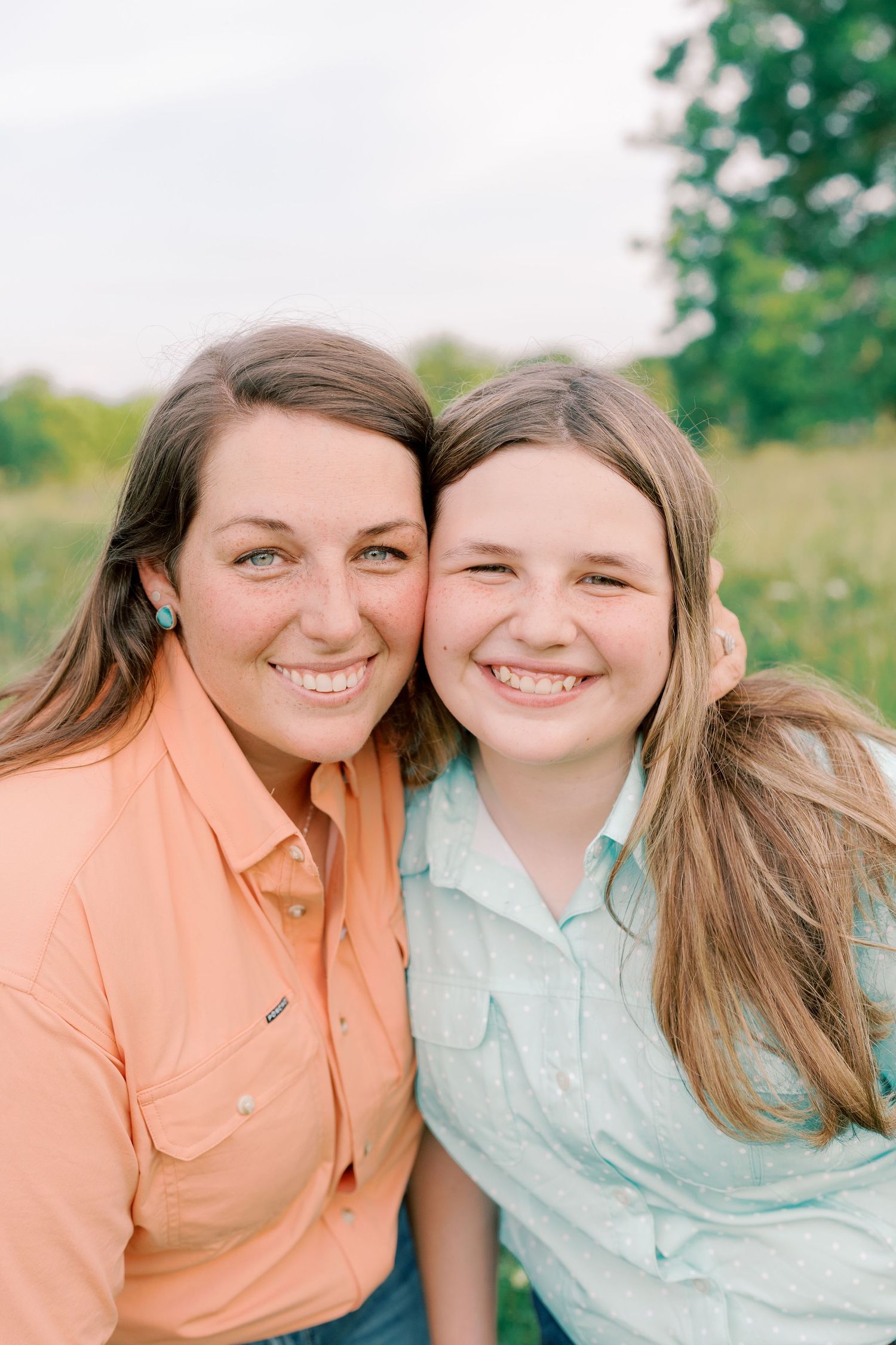 Two people in coral and mint colored shirts share a close moment outdoors.