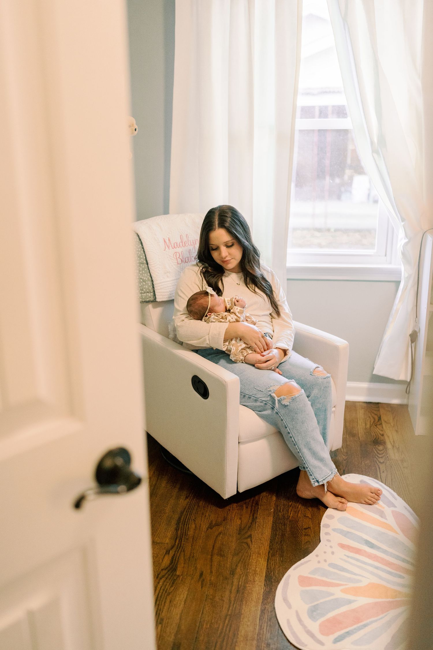 Intimate indoor portraits of a parent and baby relaxing in a white armchair.