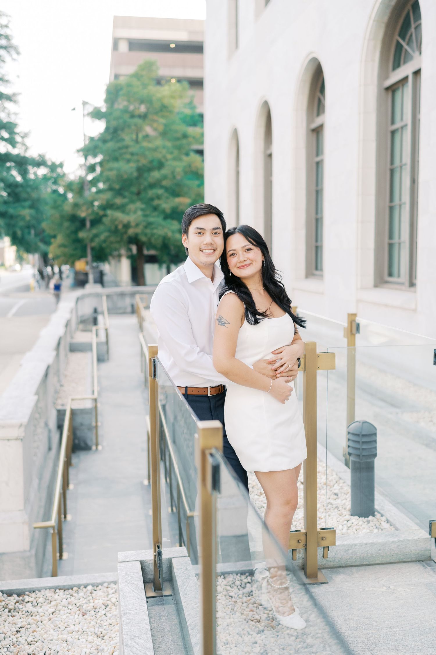 A couple takes romantic photos along a white building exterior with decorative railings.