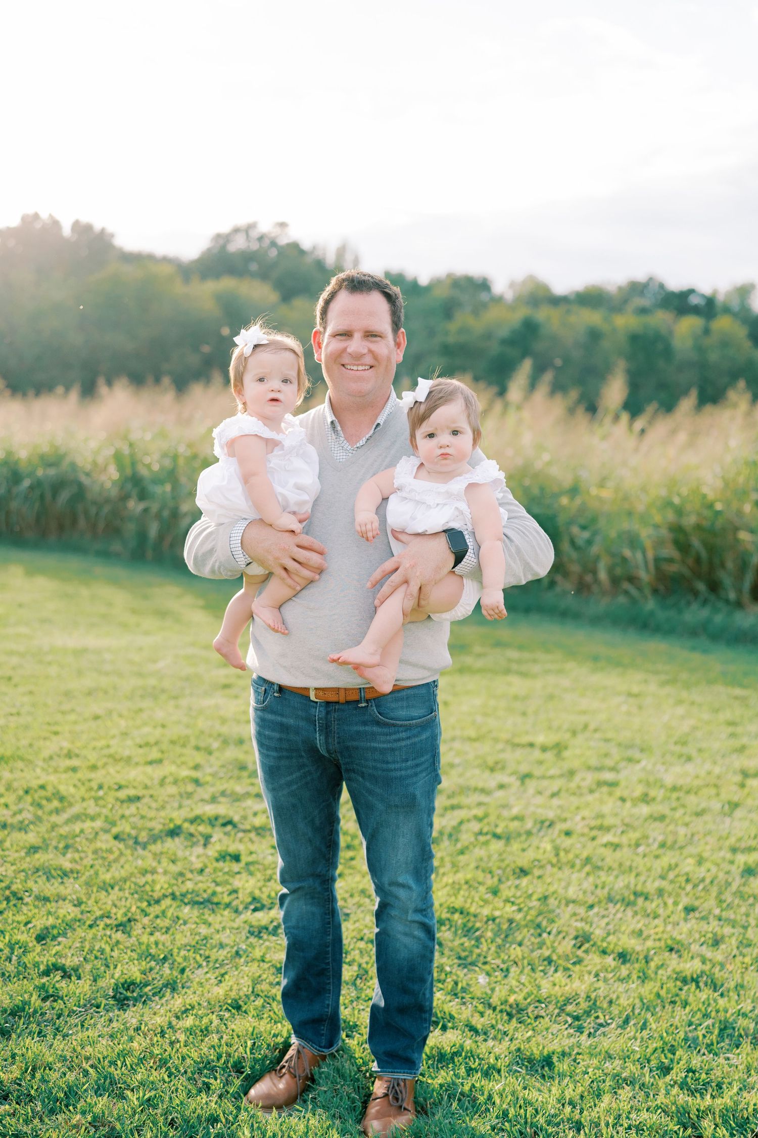 Family portrait session in a green field during golden hour with everyone dressed in coordinating outfits.