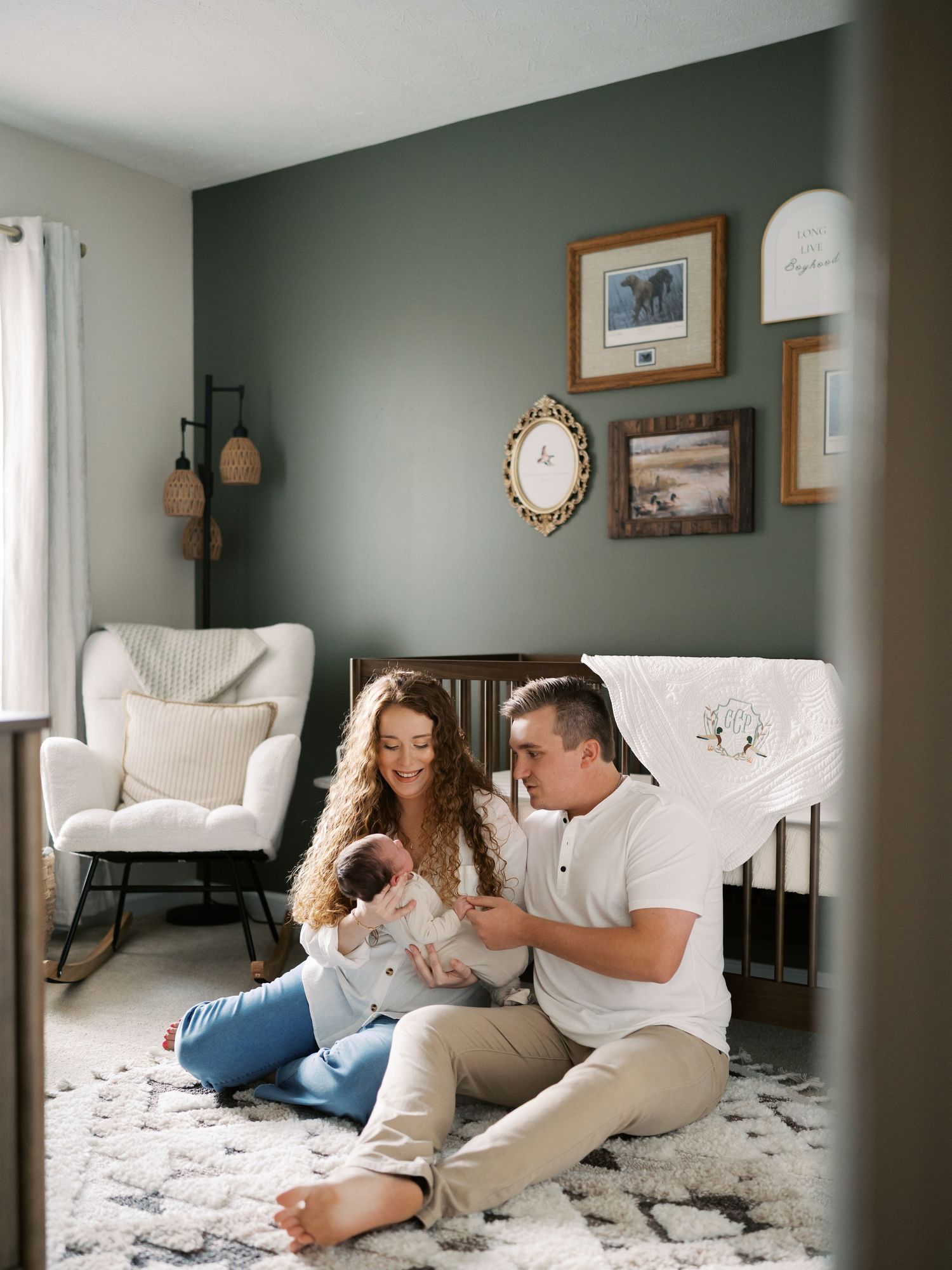 Family relaxing together on a plush white carpet in a modern nursery with decorative wall art.