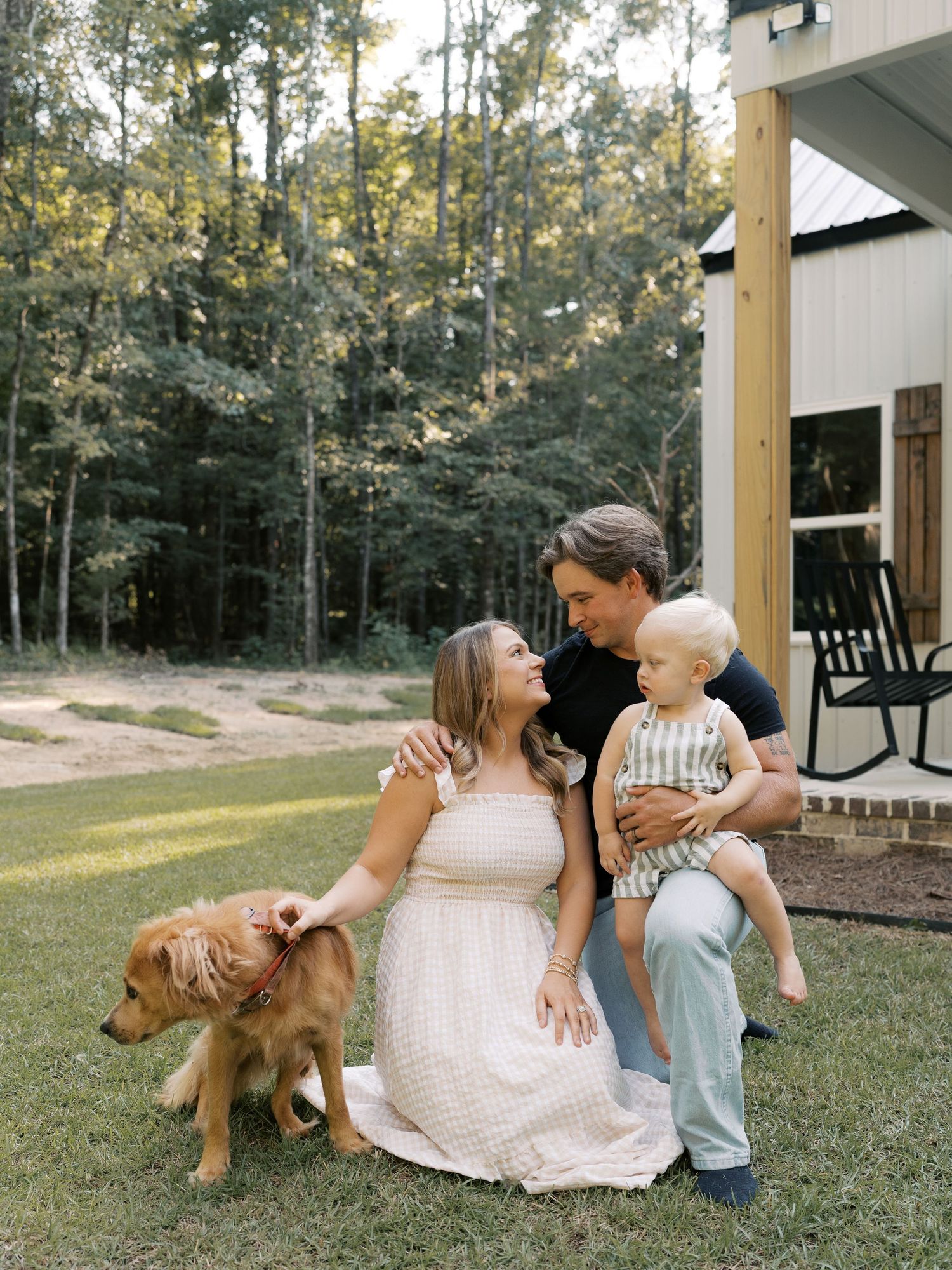 Family shares tender moments on their lawn while their dog plays nearby.
