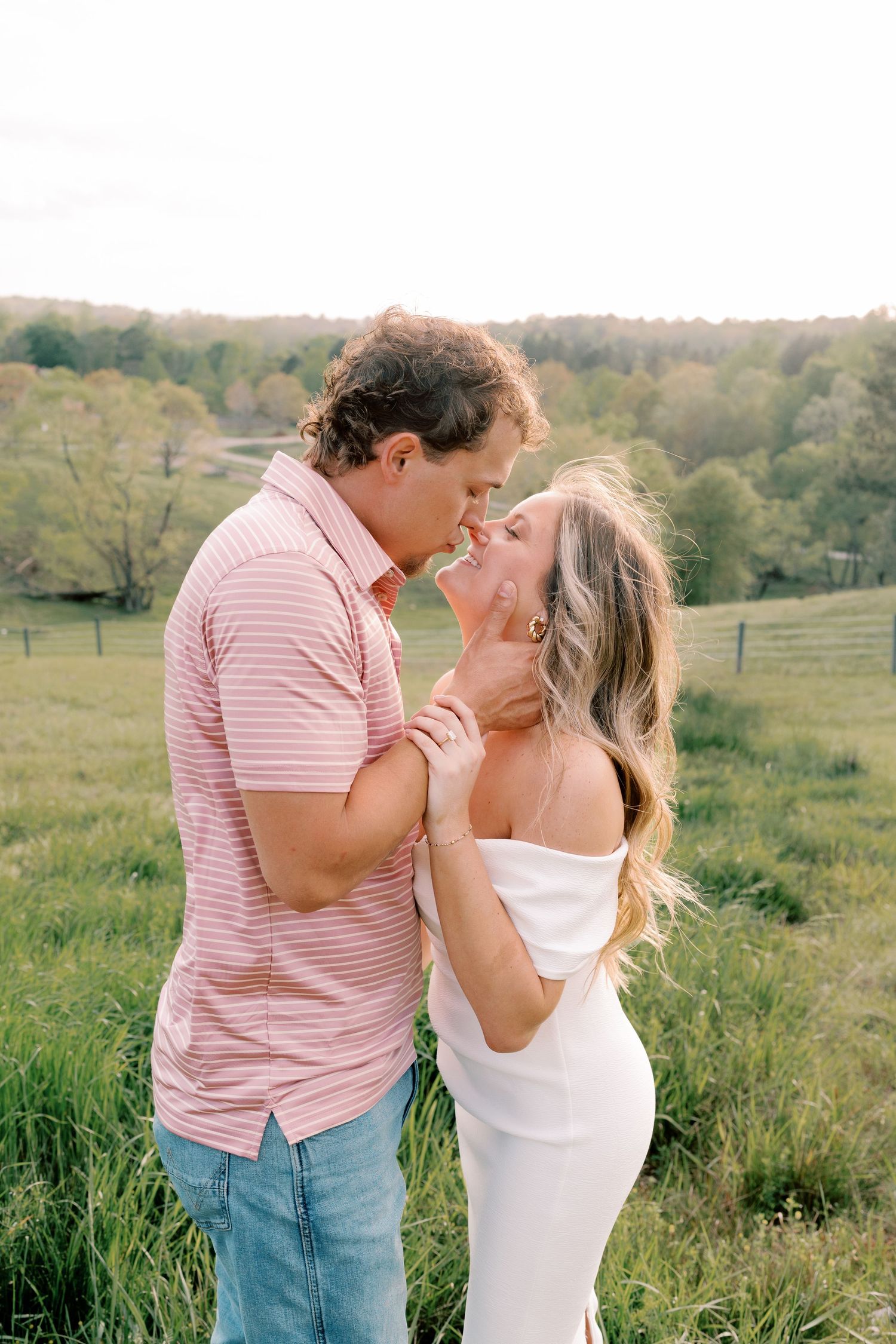 Couple shares intimate moments against backdrop of rolling green hills and countryside.