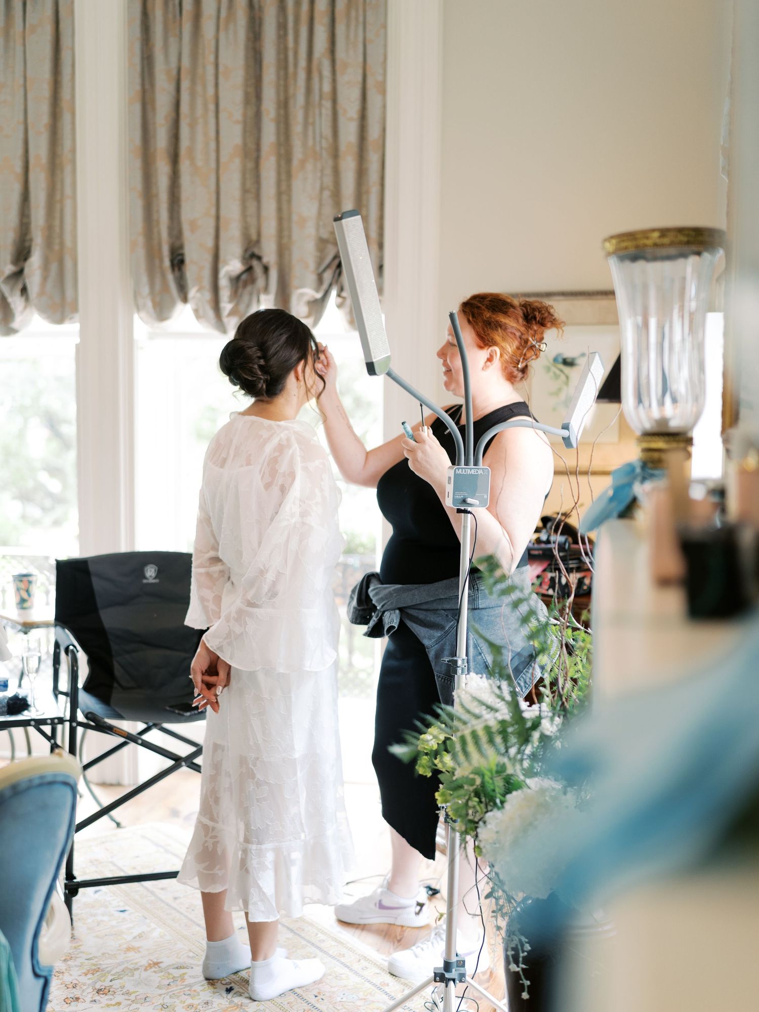 Wedding preparation scene showing people getting ready in a bright interior room with curtains.