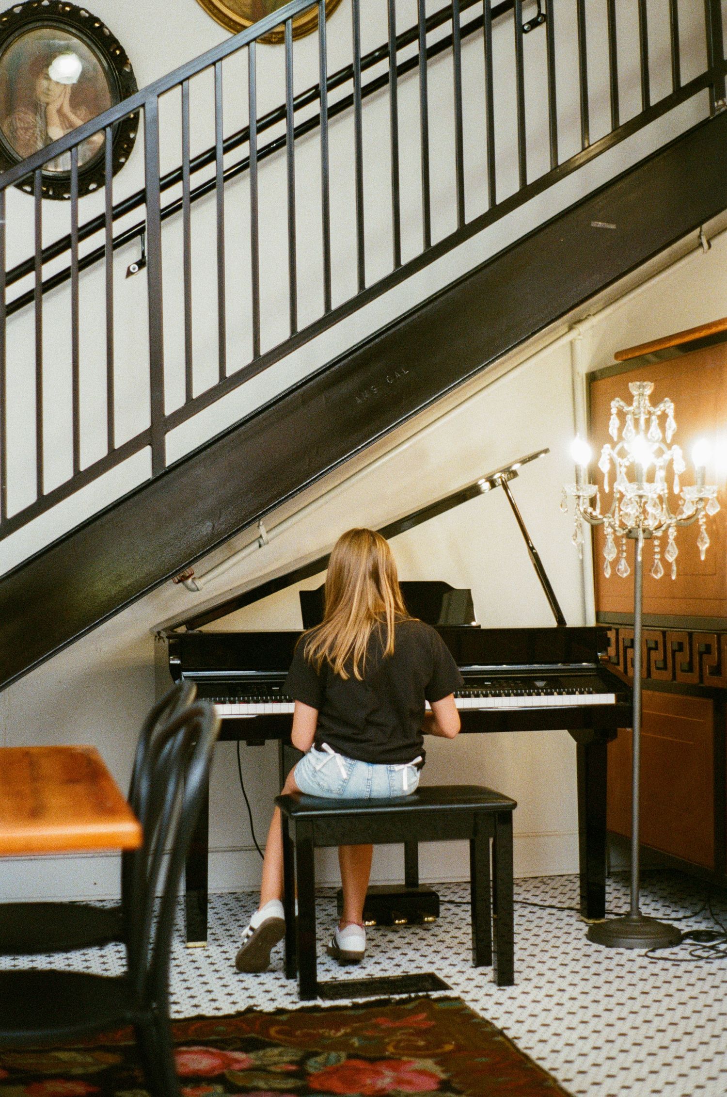 Person playing piano under elegant chandelier lighting in a room with black and white tile floor.