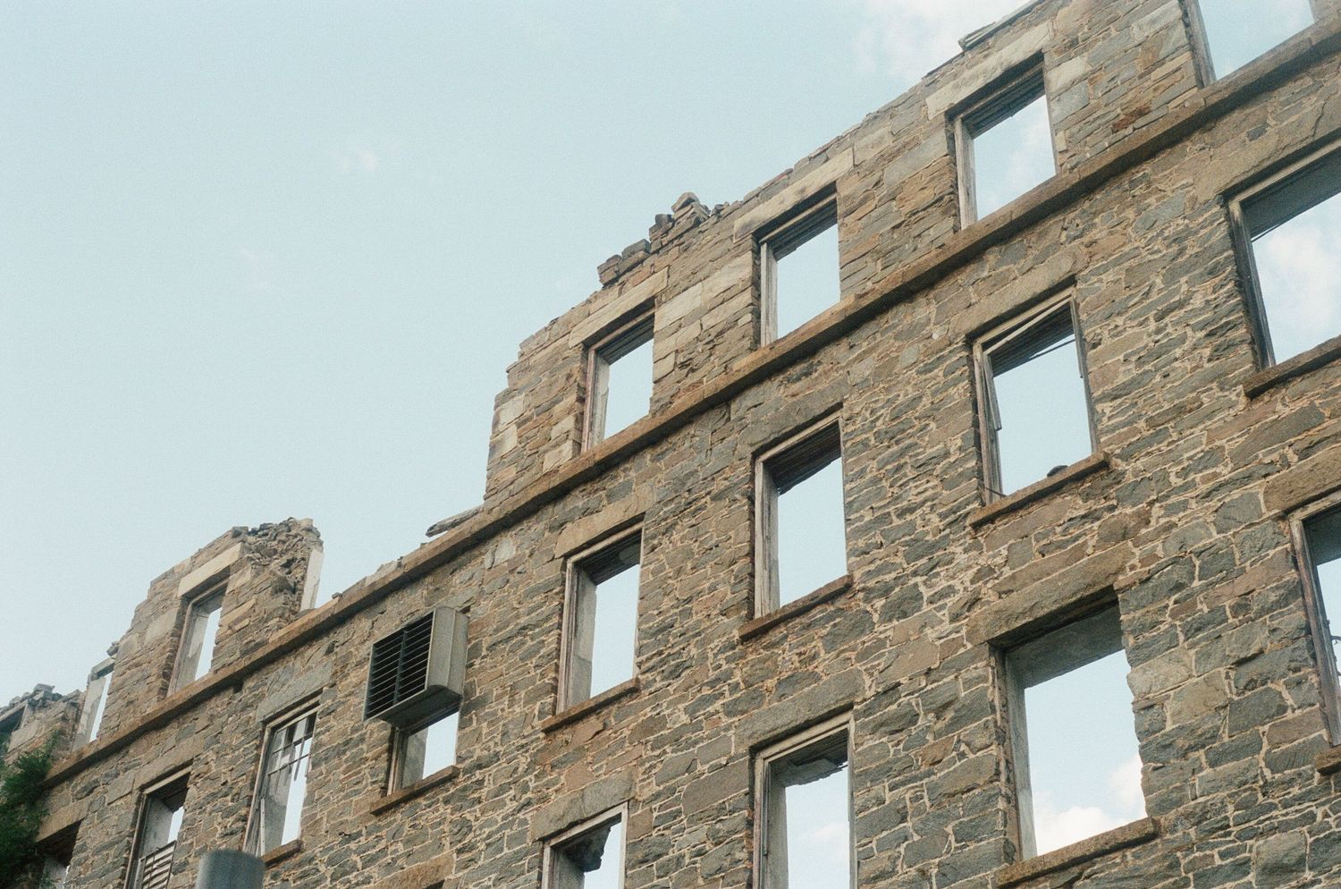 Stone castle wall ruins with multiple window openings against blue sky.