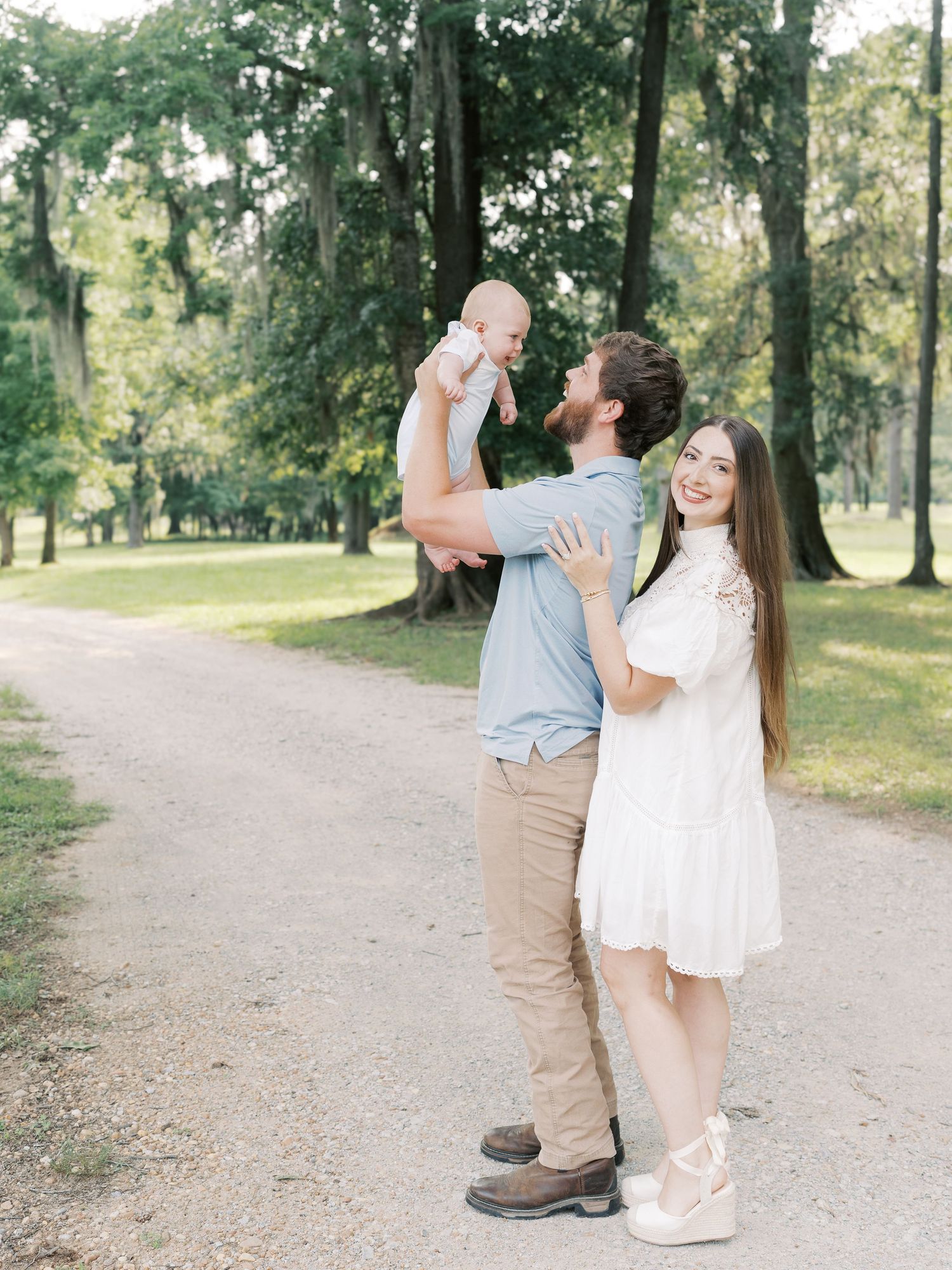 A family shares playful moments together while walking on a dirt path surrounded by trees.