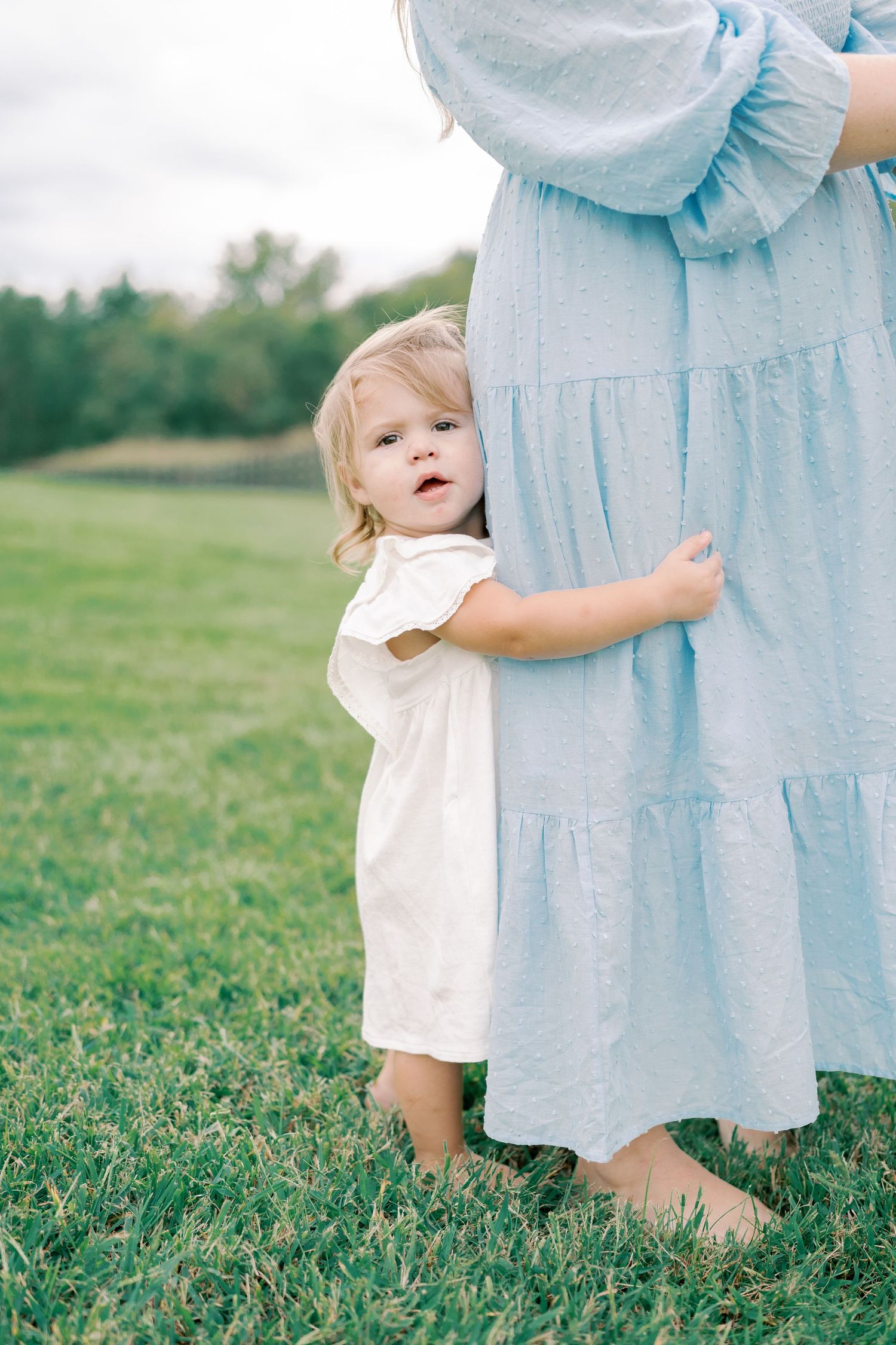 Candid moment of light blue dress and small feet in grassy field.