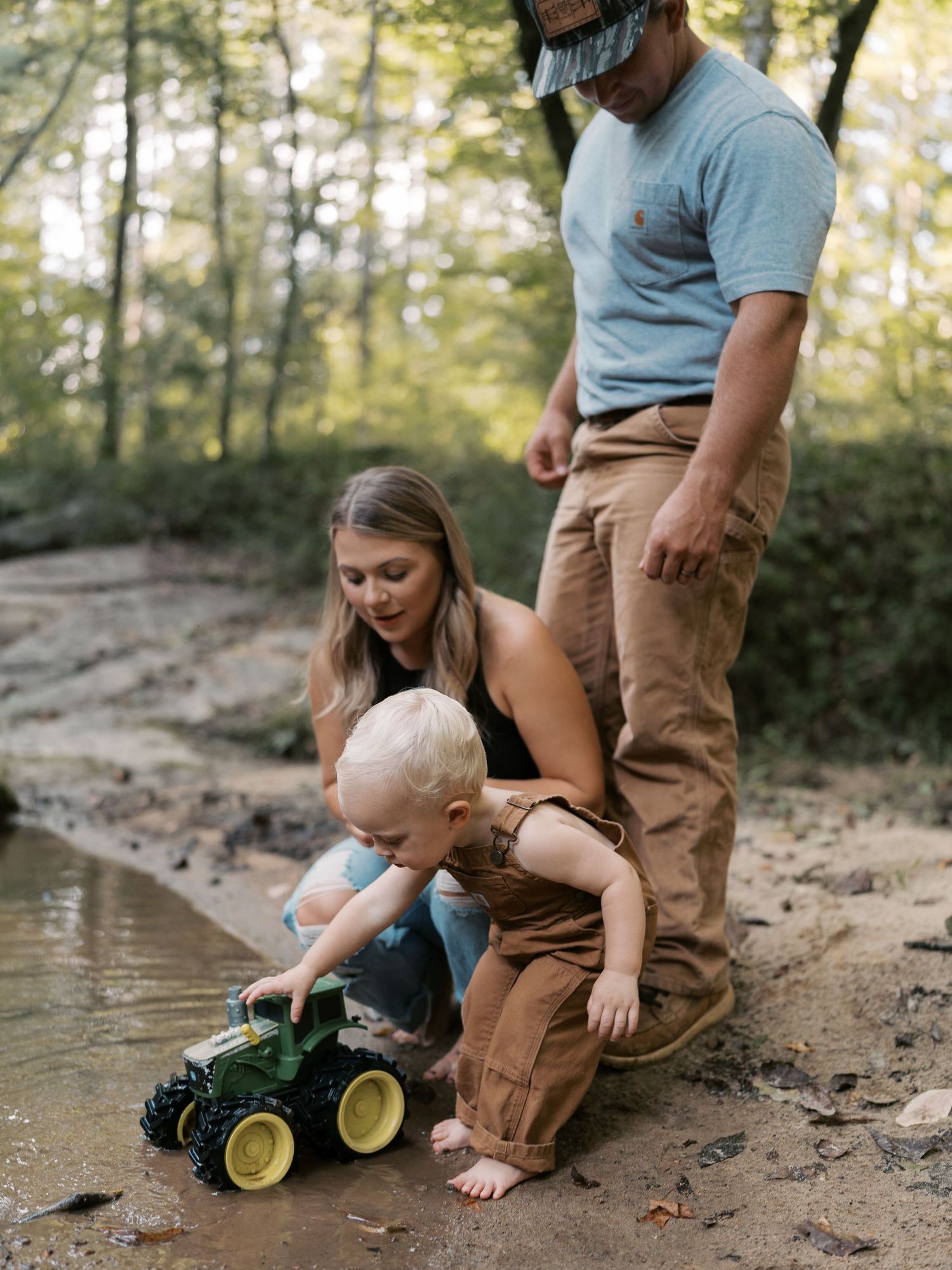 A child plays with a toy tractor while exploring nature with family.
