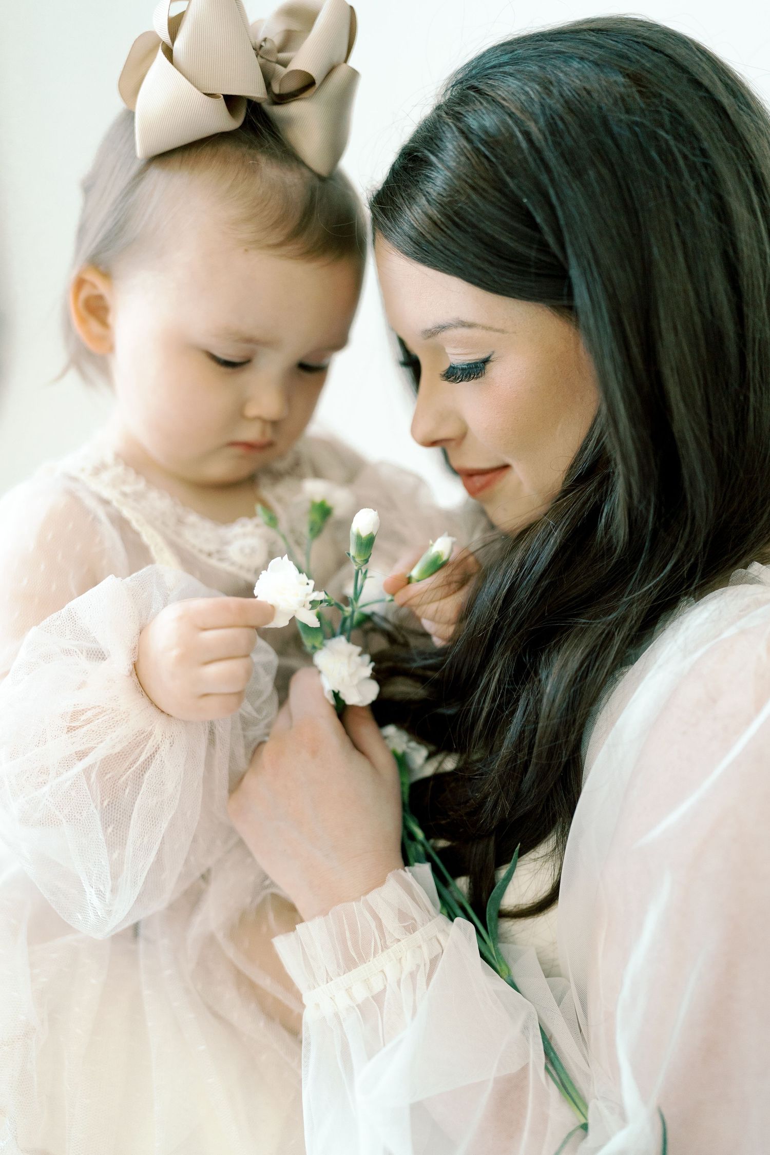 A tender moment with flowers as a baby in pink tulle dress explores delicate white blooms.
