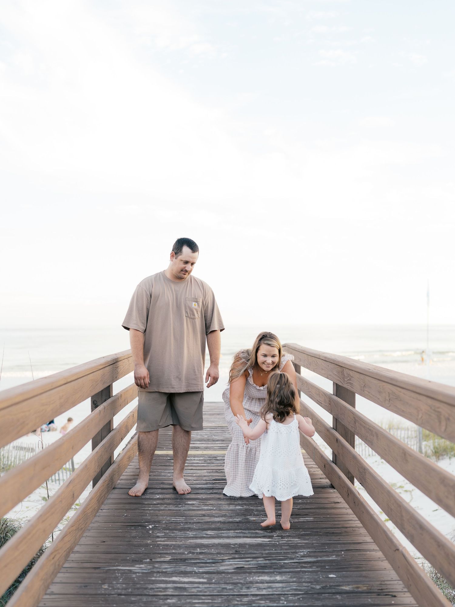 A family walks together on a wooden boardwalk near the beach.