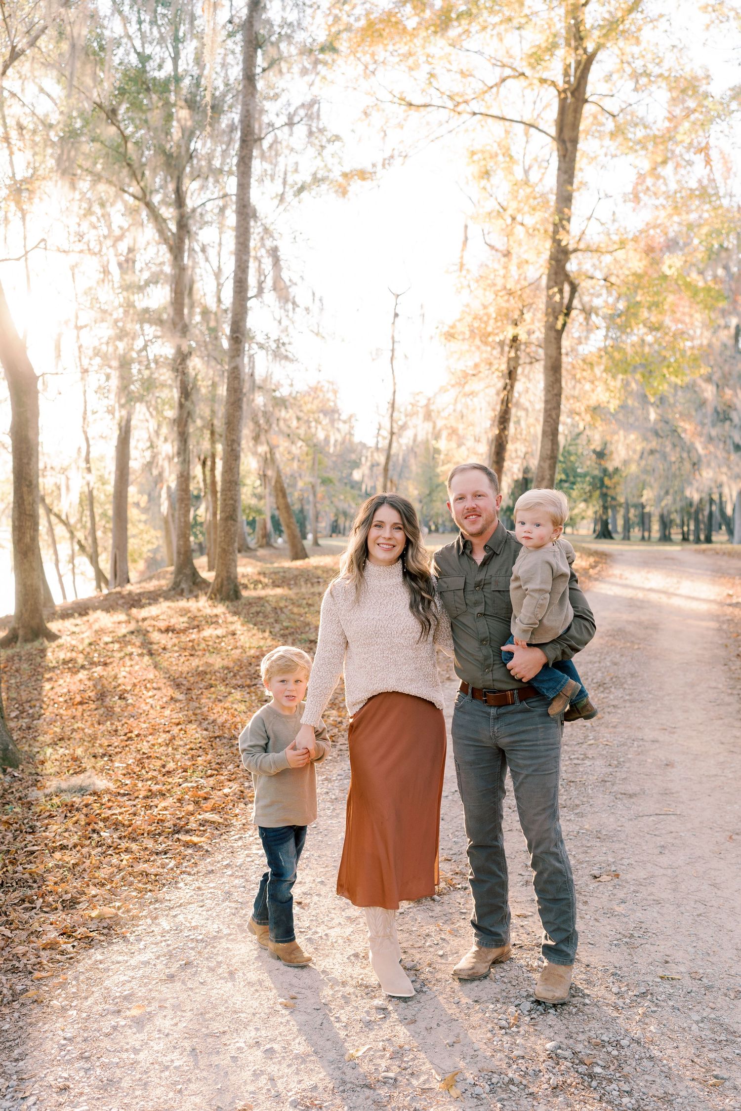 Family standing together on leaf-covered path during golden hour in autumn.