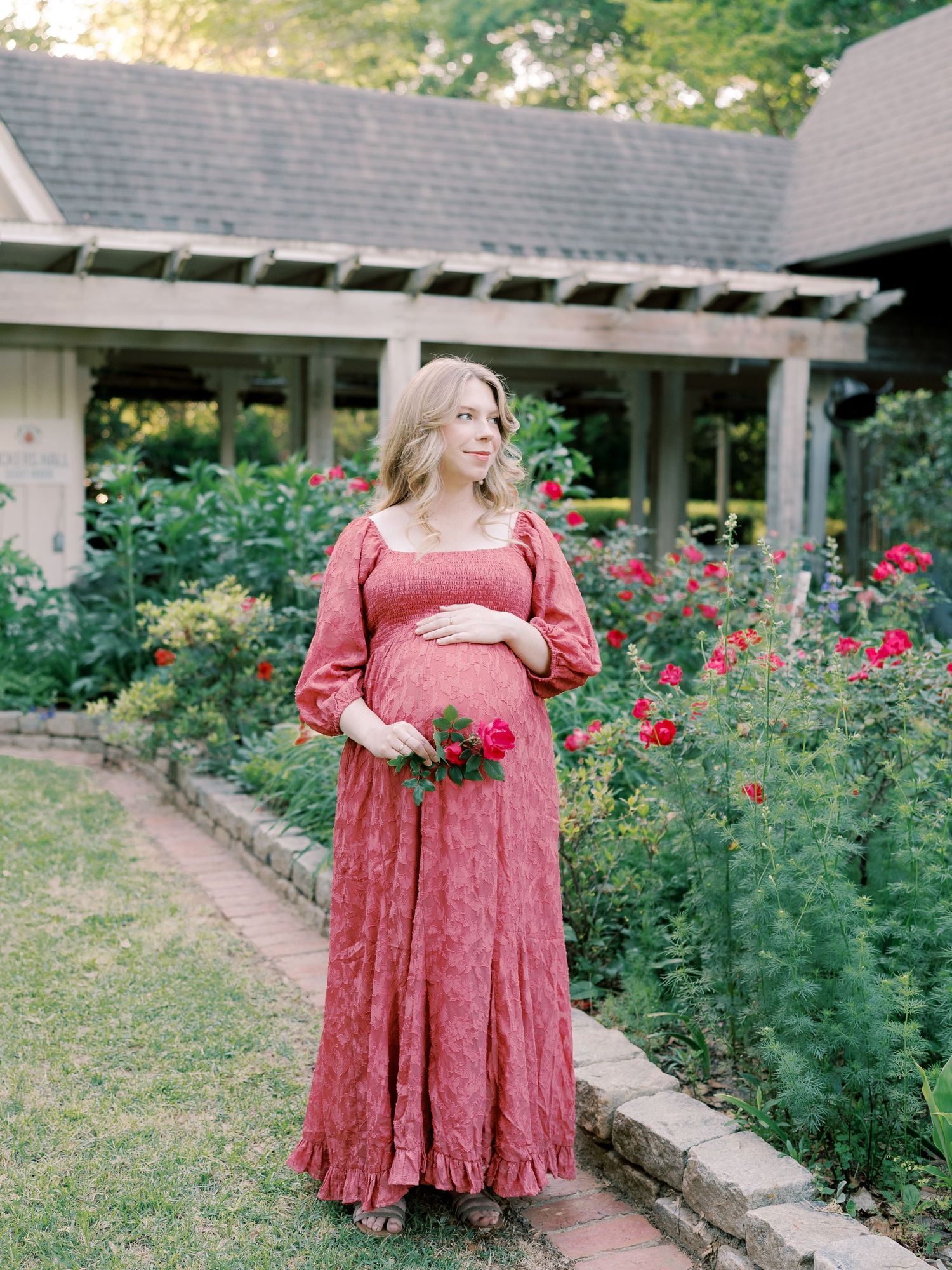 A pink floral dress is showcased in a garden setting with blooming roses and architectural elements.