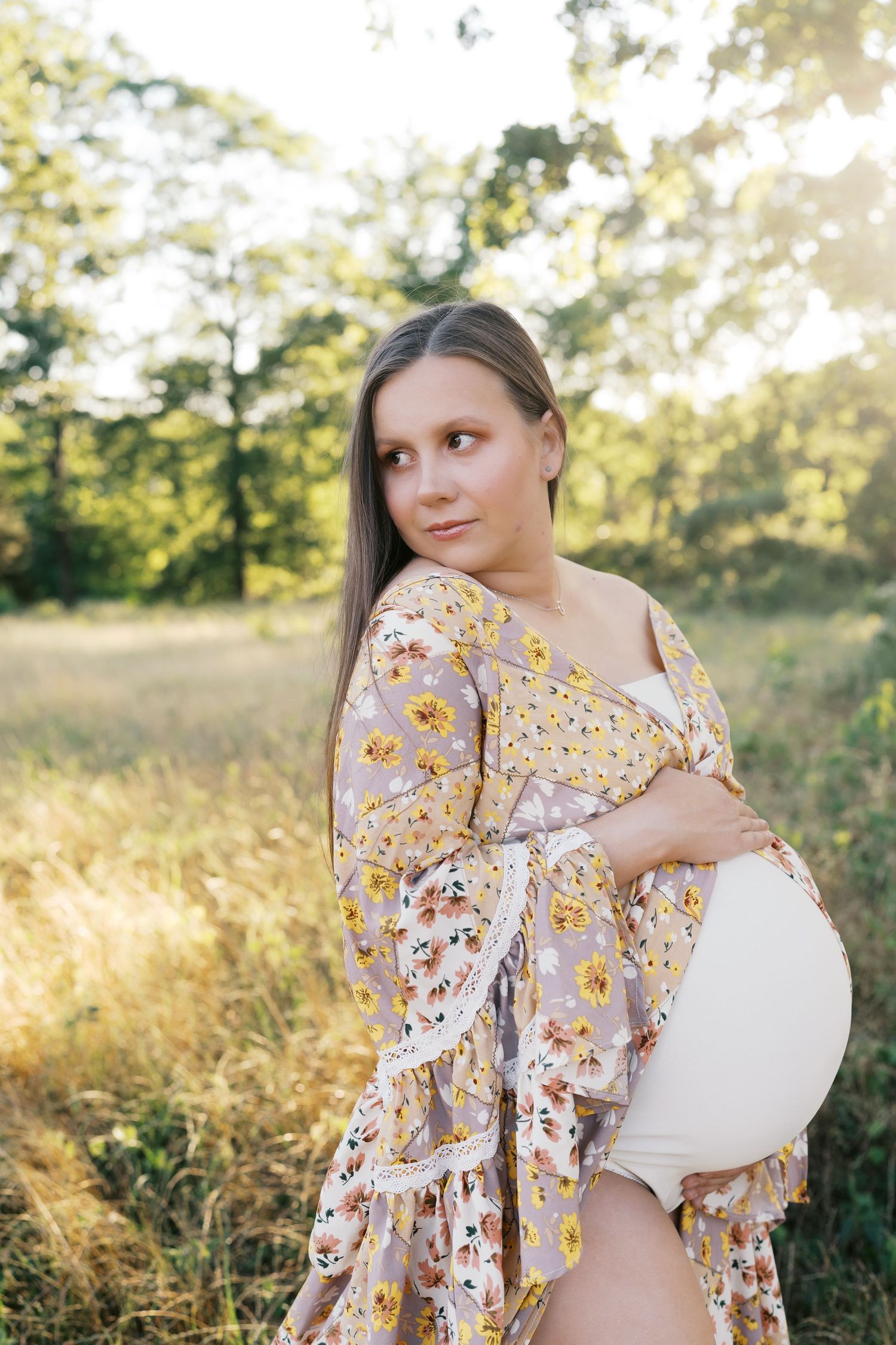 Romantic maternity photos featuring yellow floral dress in outdoor natural setting with golden sunlight.