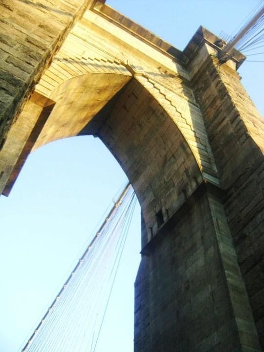 Low angle view of stone bridge arches against bright blue sky.