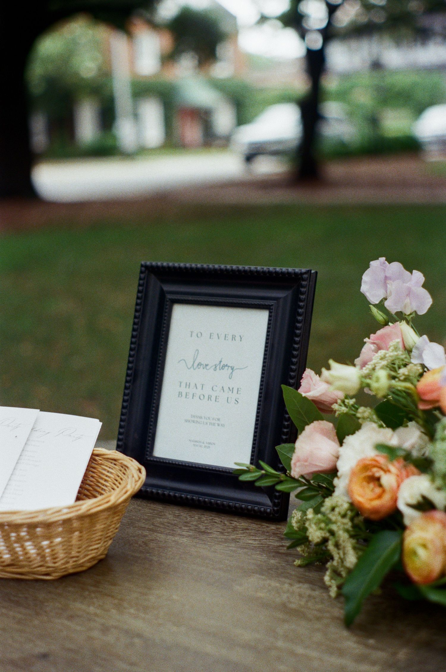 Wedding signage in black frames with floral arrangements on rustic wooden surface.